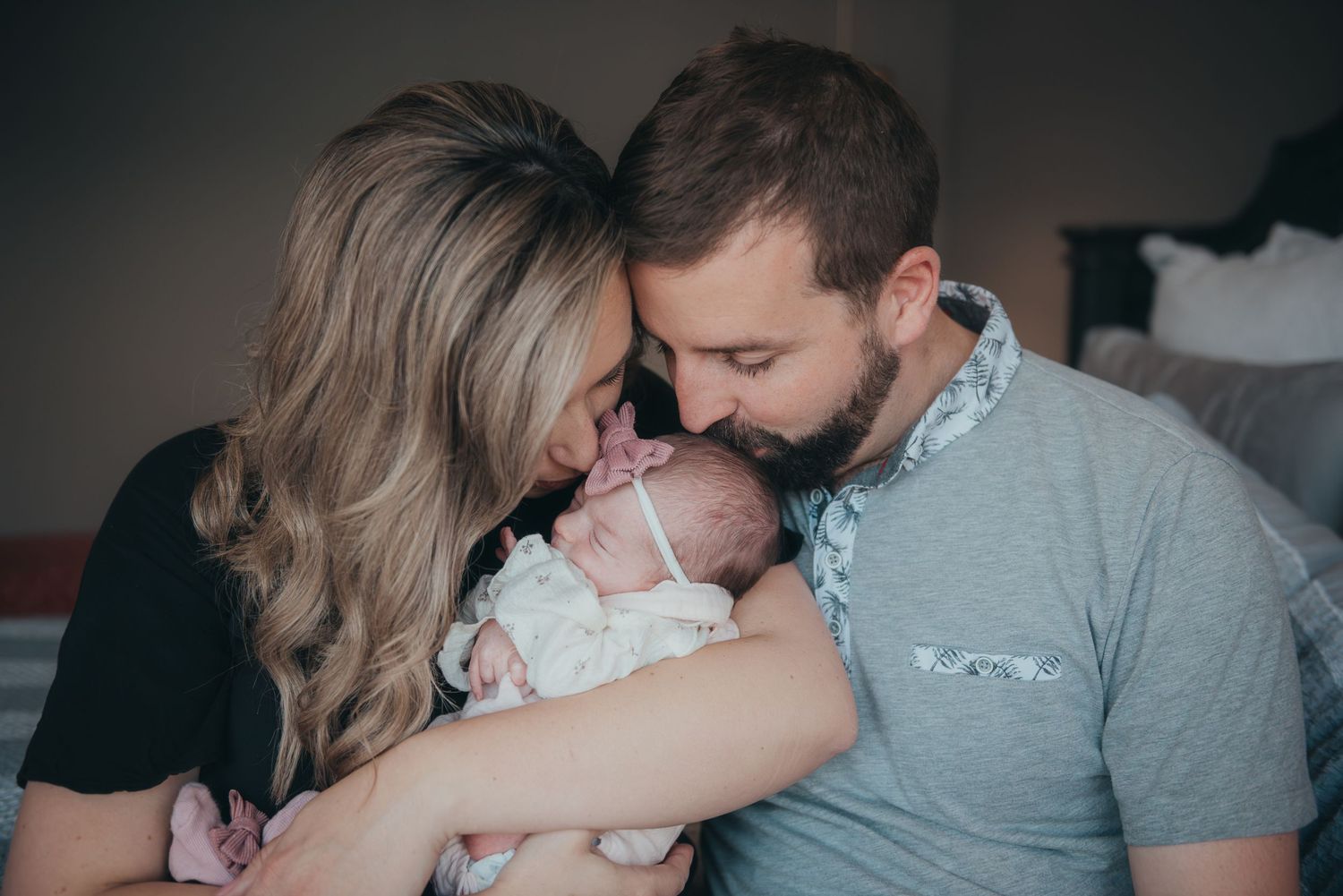 Natural lifestyle photography of parents kissing their newborn head.