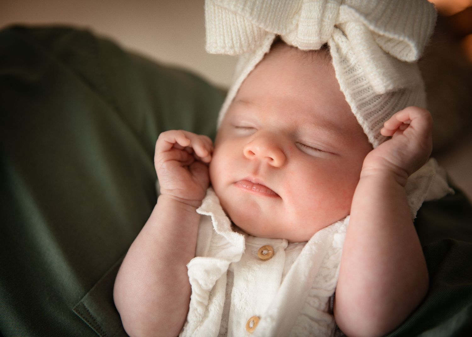 Sleeping newborn in white outfit against dark green background.