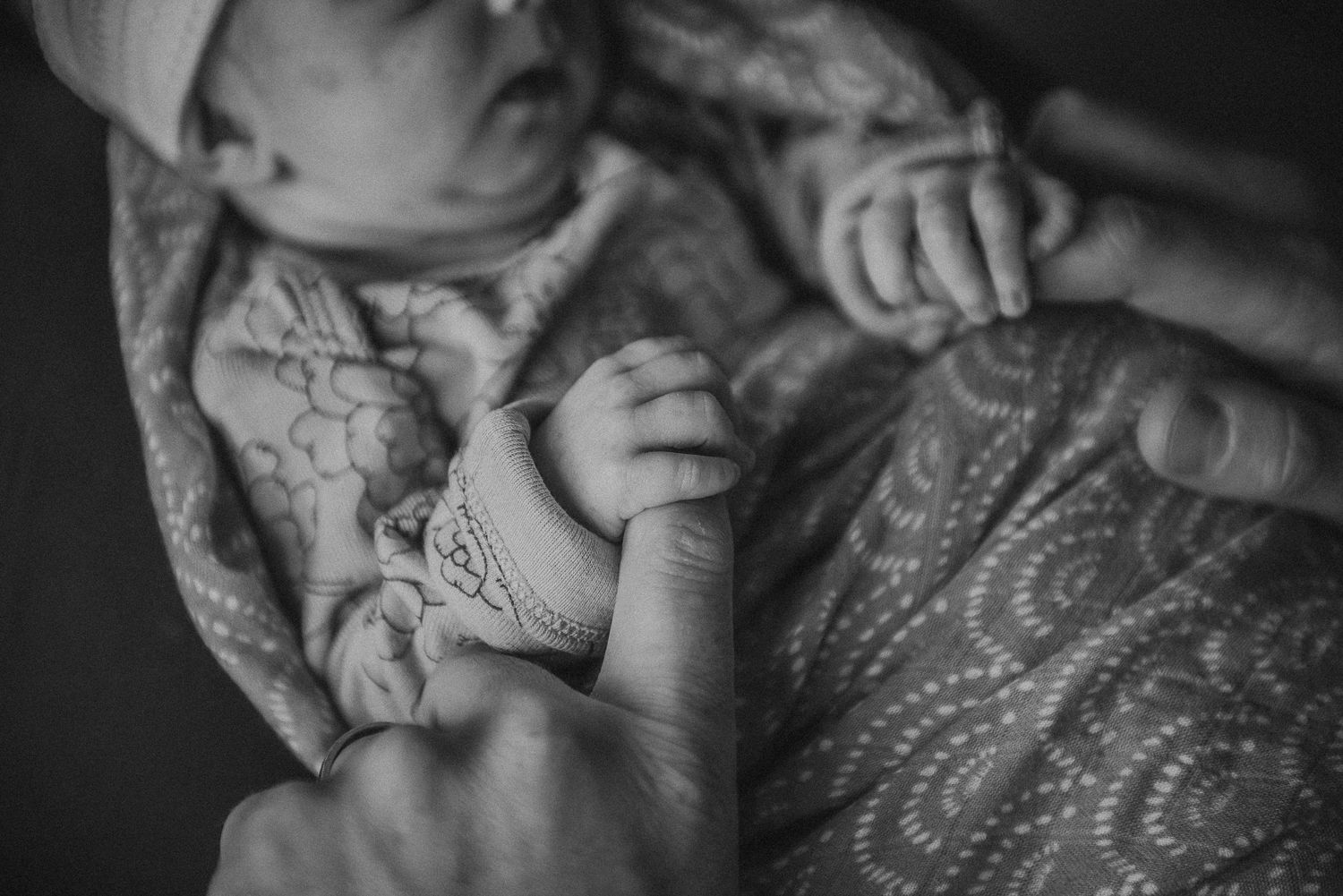 Black and white photo of a newborn baby holding dads hands during Calgary newborn photoshoot