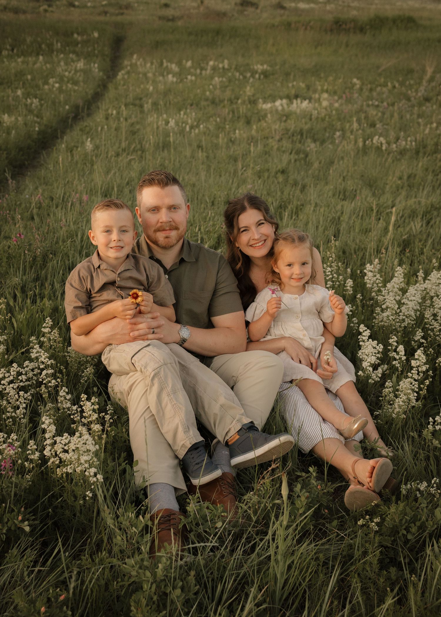 Family of four smiling at the camera sitting on a hillside for family photos in Calgary