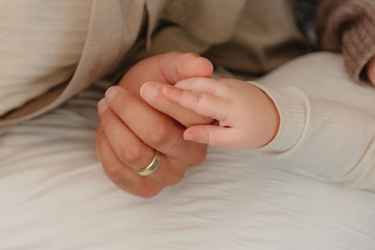 Close-up of a small baby hand gently holding an adult finger against soft beige fabric.