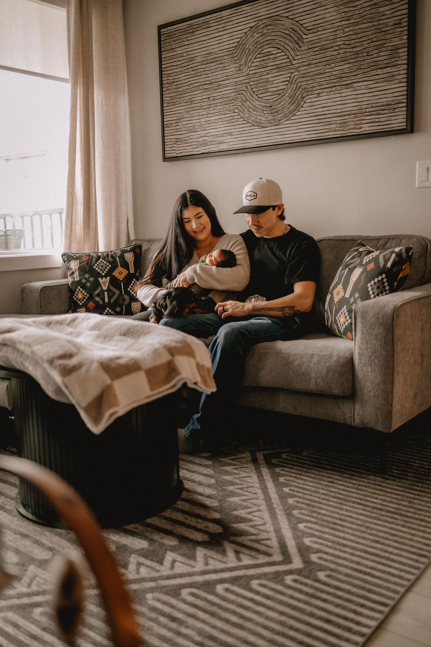 New parents sit on a gray sofa admiring their newborn baby in a cozy, modern Calgary living room.