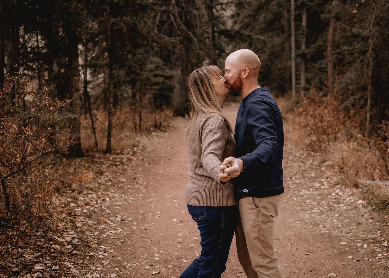 A couple shares an intimate moment on a Calgary forest path during autumn.