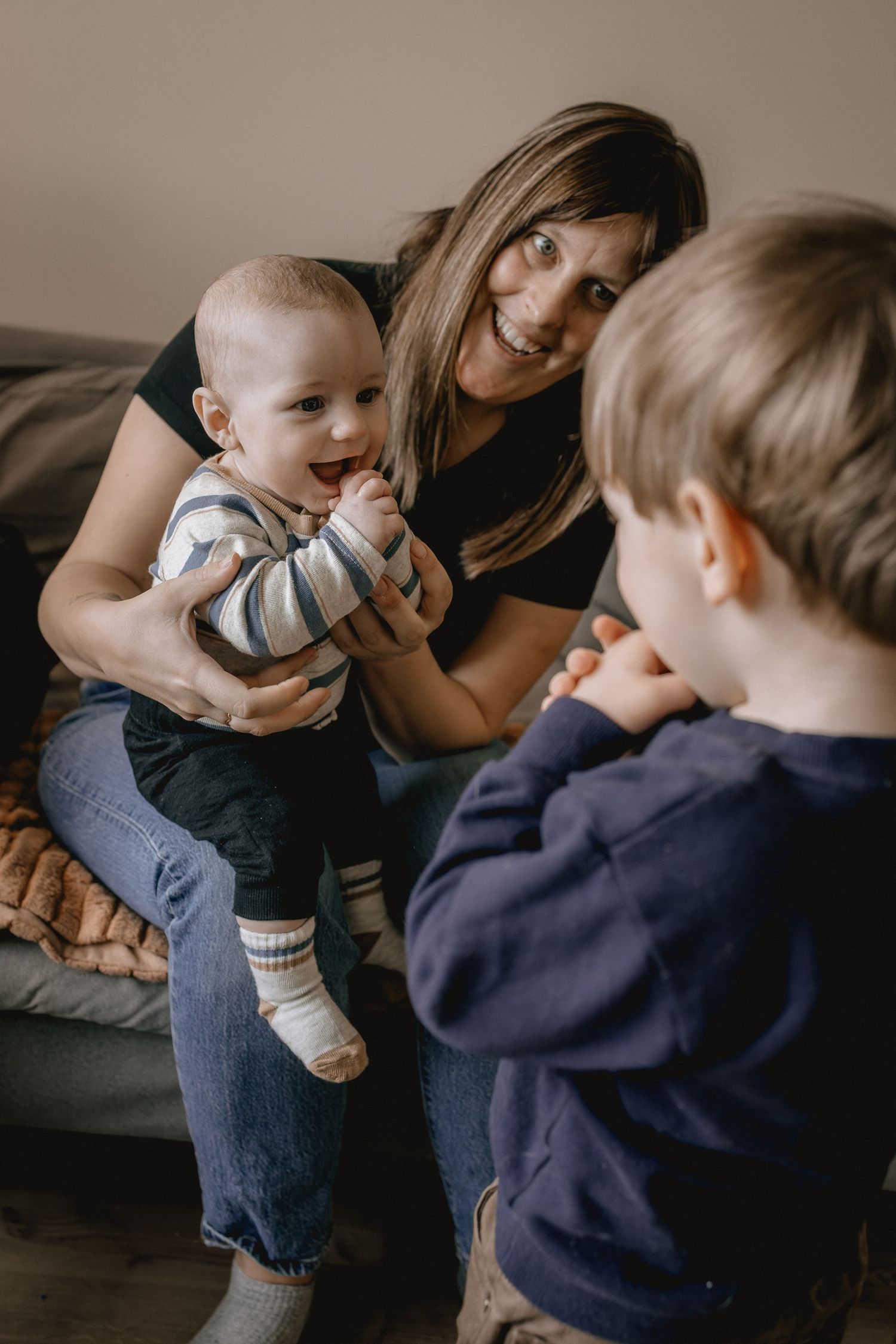 A smiling mother holds a happy baby while a young boy looks on during a warm family photography session in Calgary, AB