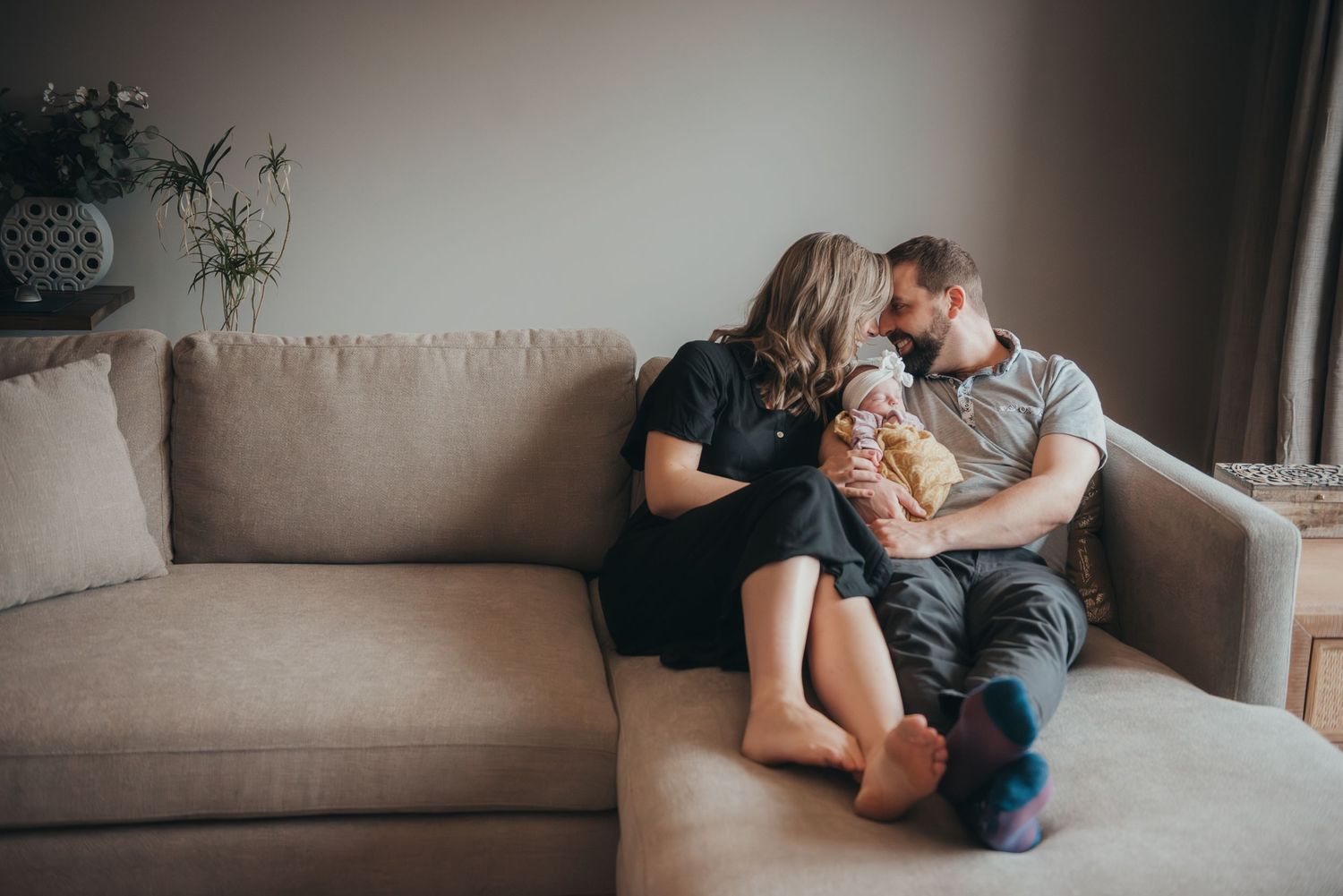 Lifestyle Calgary newborn photography session capturing intimate moments between parents on gray couch in natural light.