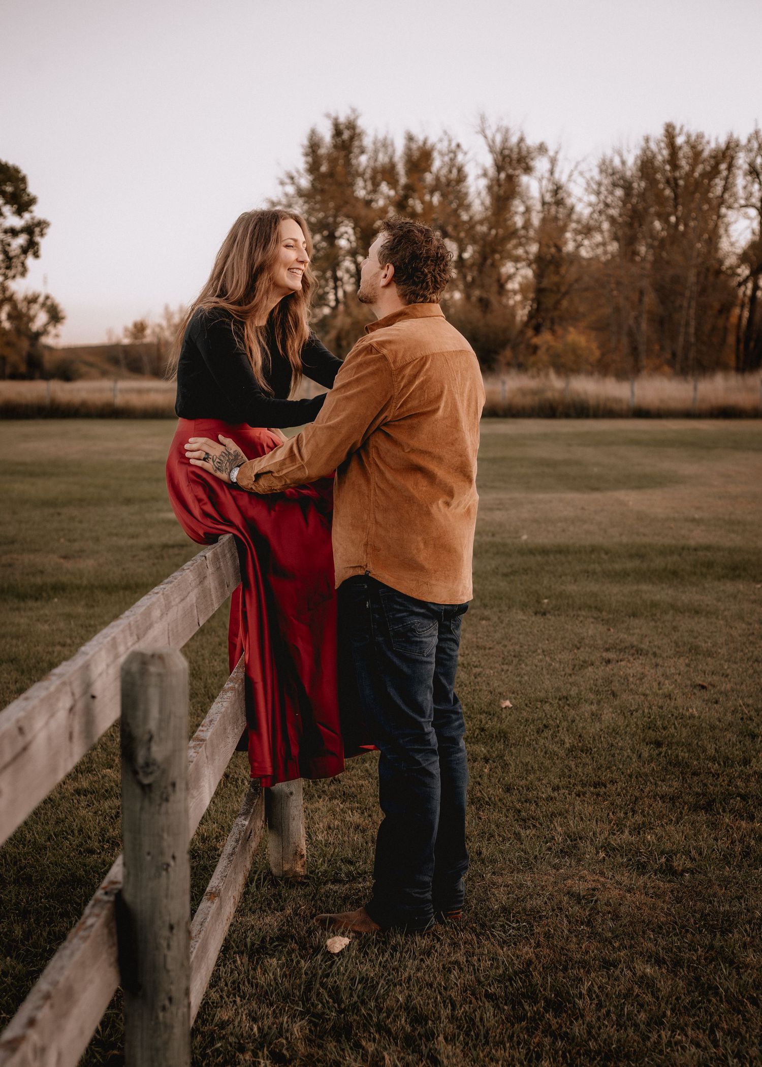 A couple shares a romantic moment along a rustic wooden fence at sunset during a photo session..