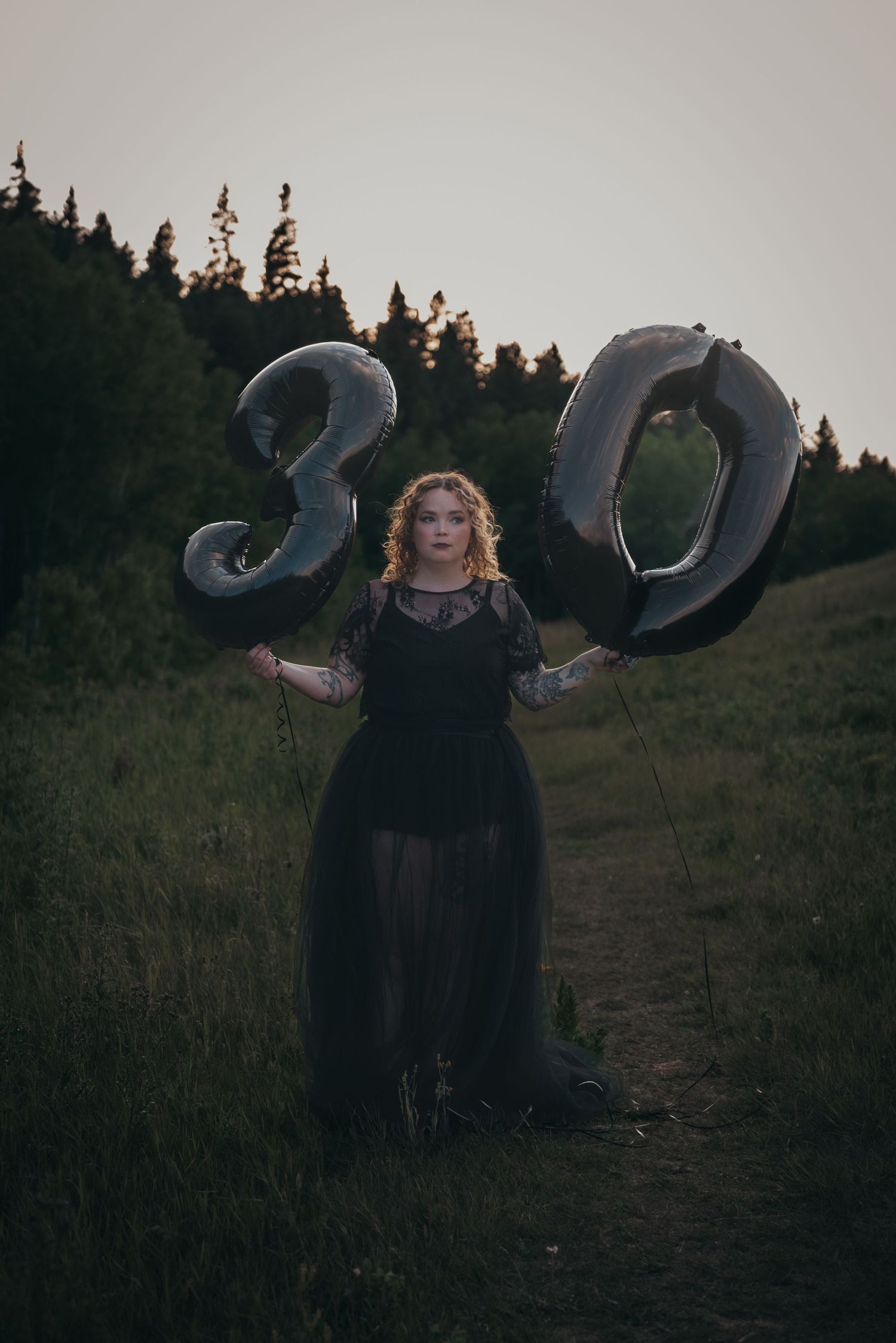 Woman in black dress holding silver number 30 balloons in a Calgary field at dusk celebrating her 30th birthday.