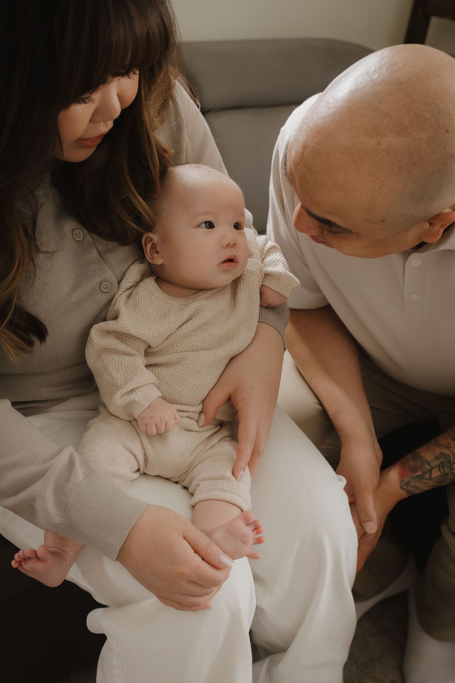 Calgary photographer captures a couple sitting together, lovingly cradling their newborn baby dressed in a neutral onesie.