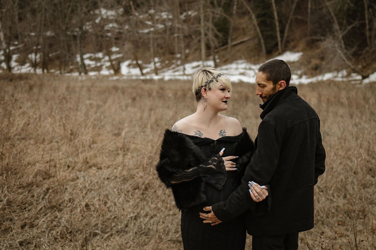 Couple in black winter attire sharing a romantic moment in a snowy field during an outdoor engagement session.