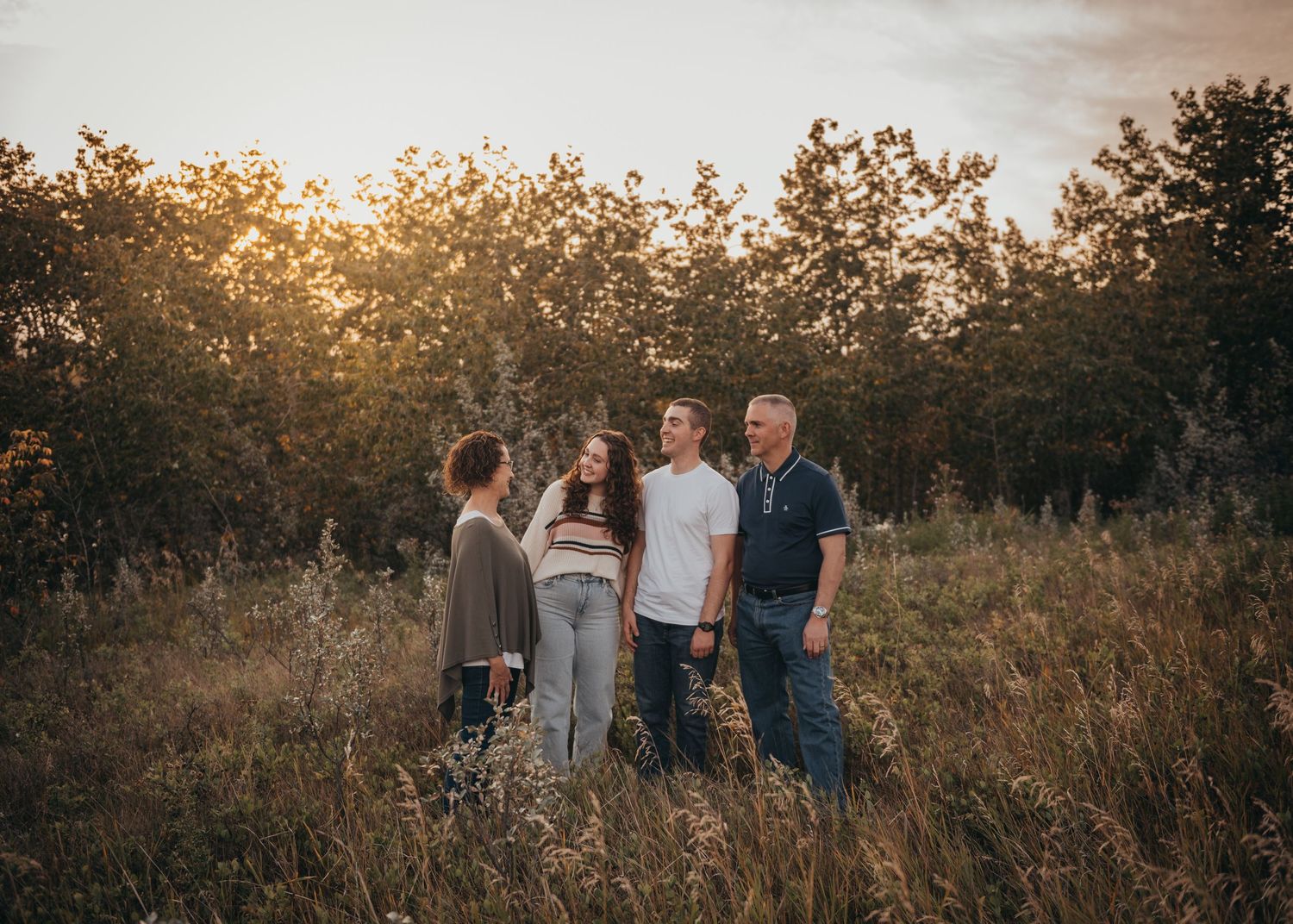 Family of four standing in golden hour sunlight among tall grass and trees outdoor Calgary