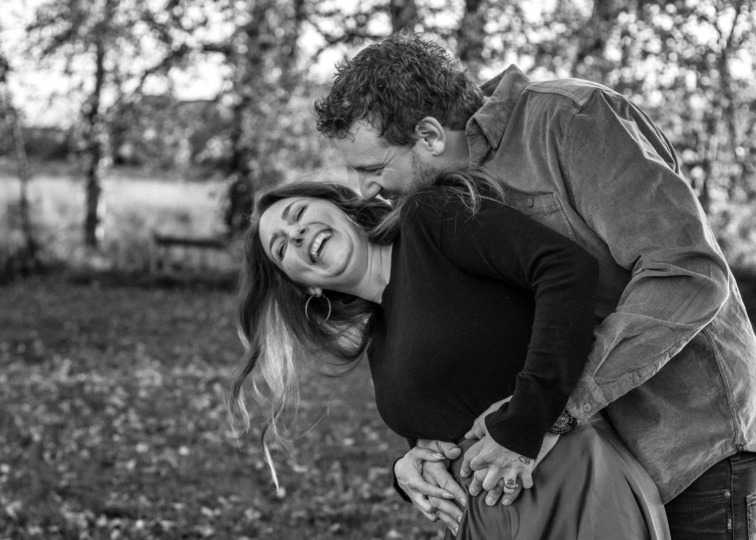 A black and white portrait of a couple sharing a lighthearted moment outdoors in rural High River, AB.