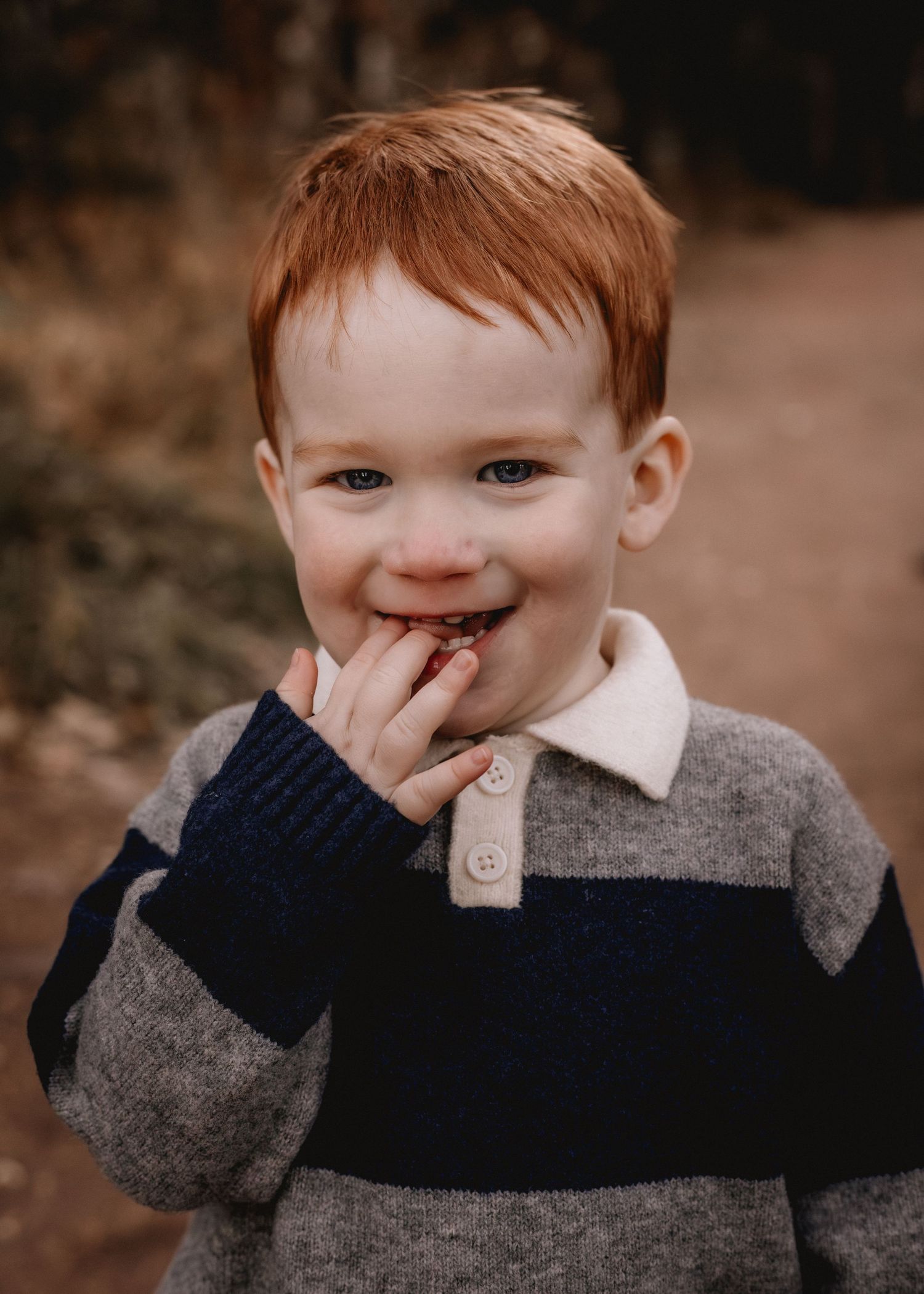 A young child in a striped sweater smiles playfully while touching their face.