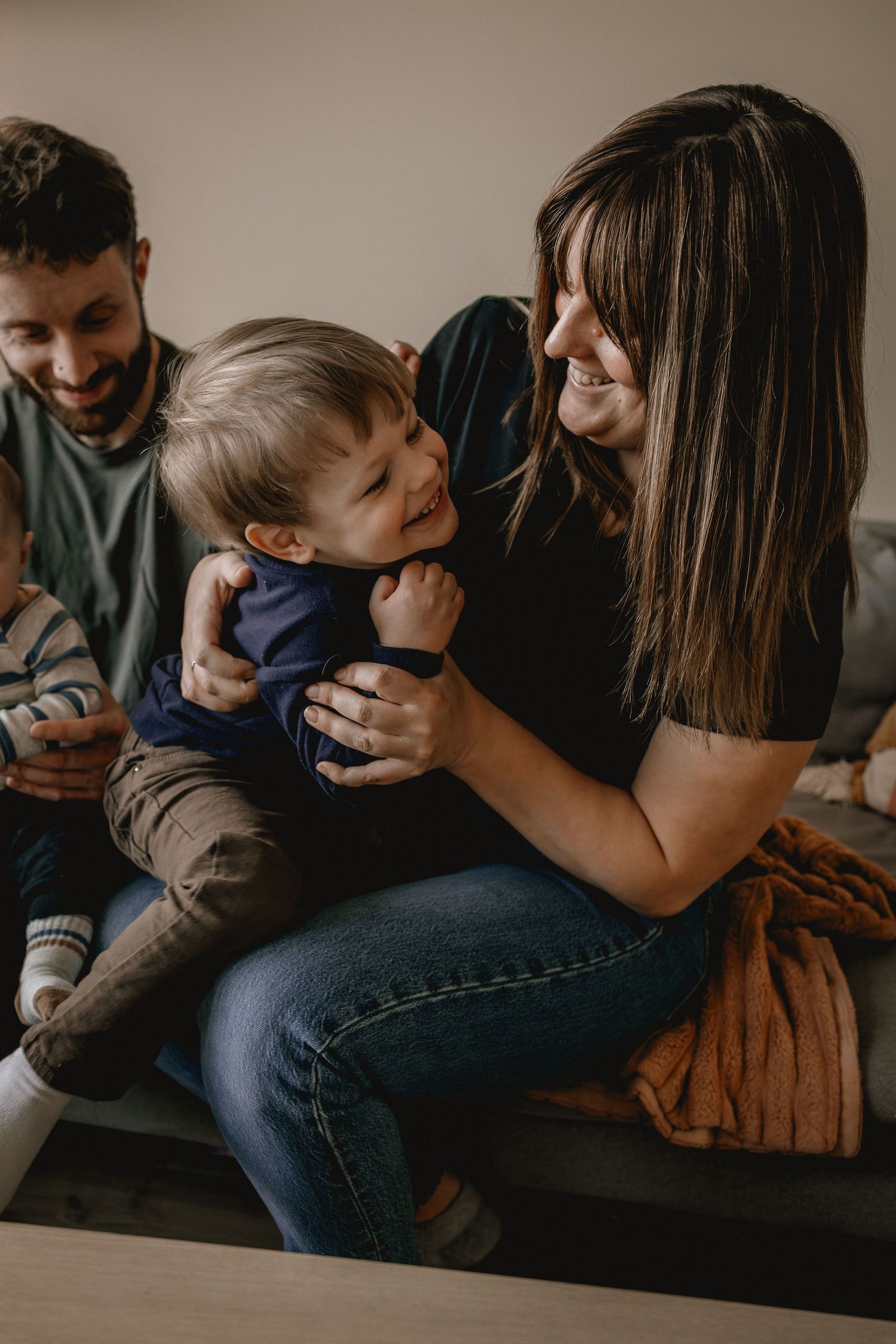 A joyful family moment with a laughing toddler on mom's lap while dad smiles warmly in a cozy home setting.