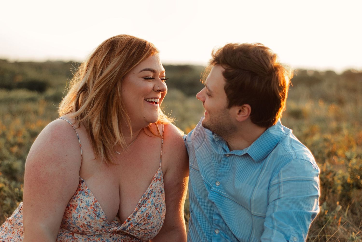 Couple smiling and laughing together outdoors in golden hour sunlight in a field.
