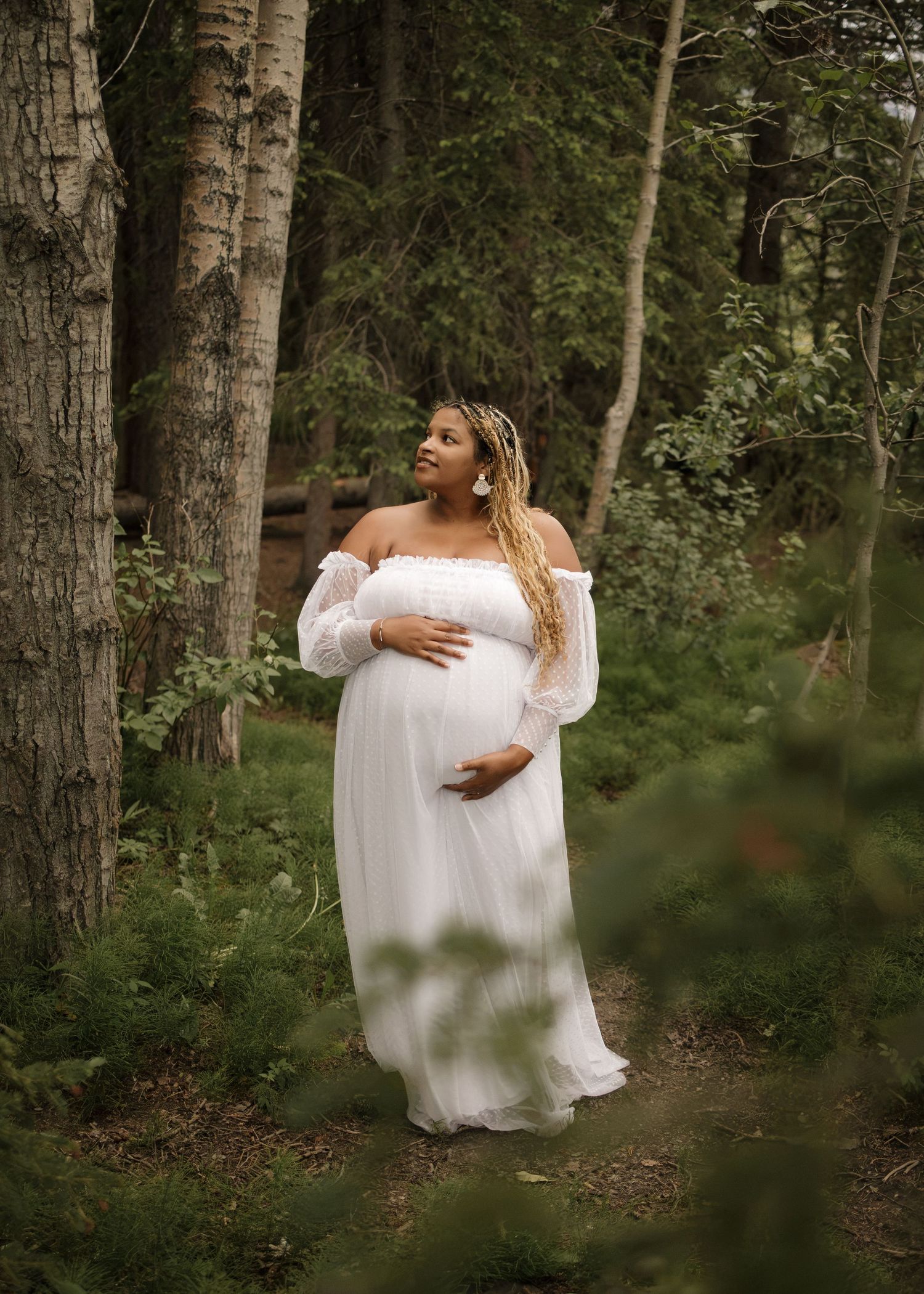 Woman hugging her pregnant belly looking into the trees during Calhary maternity session