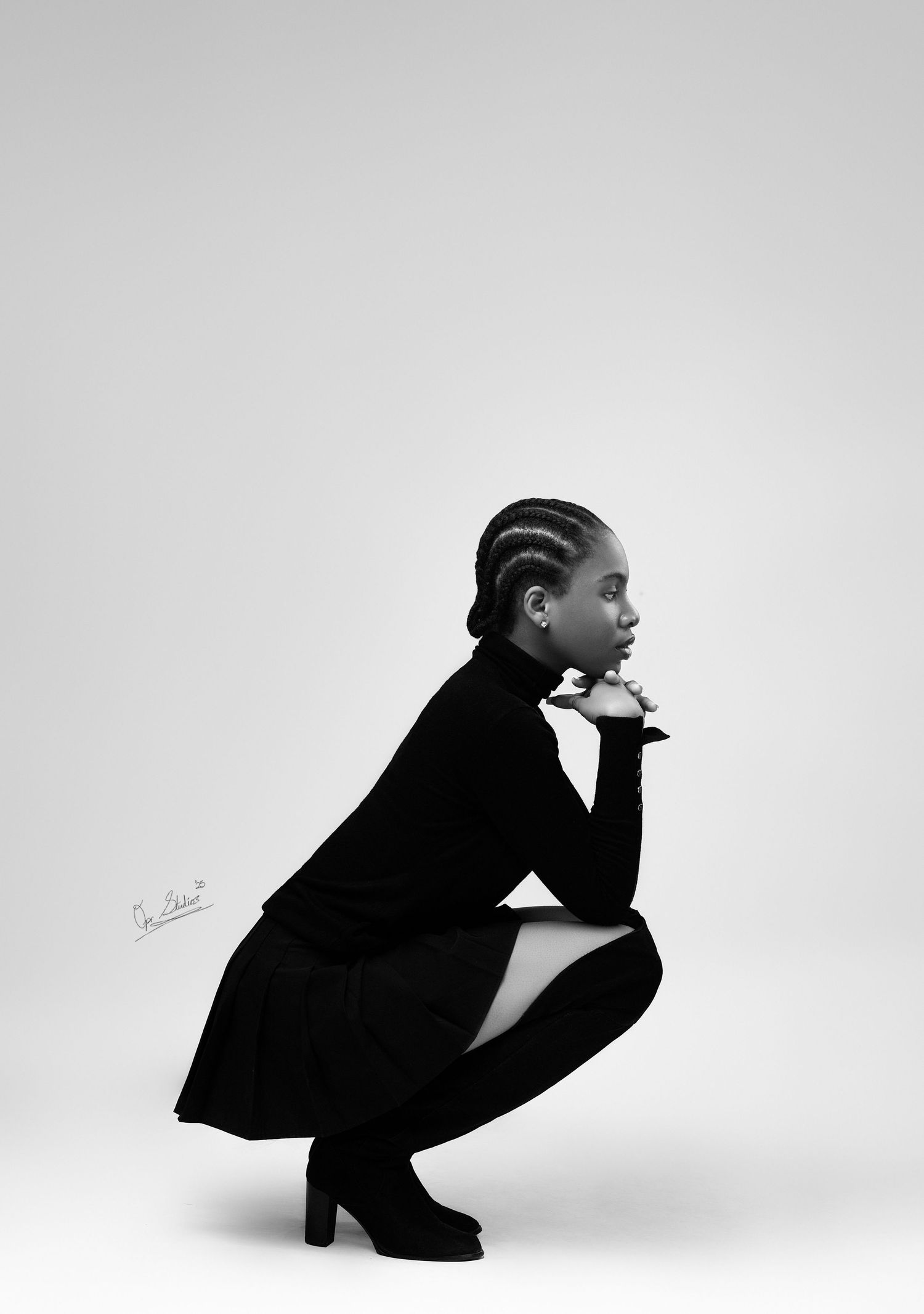A B & W portrait of a beautiful Nigerian model squatting on the studio floor in a black turtle neck, black skirt and black knee high boots