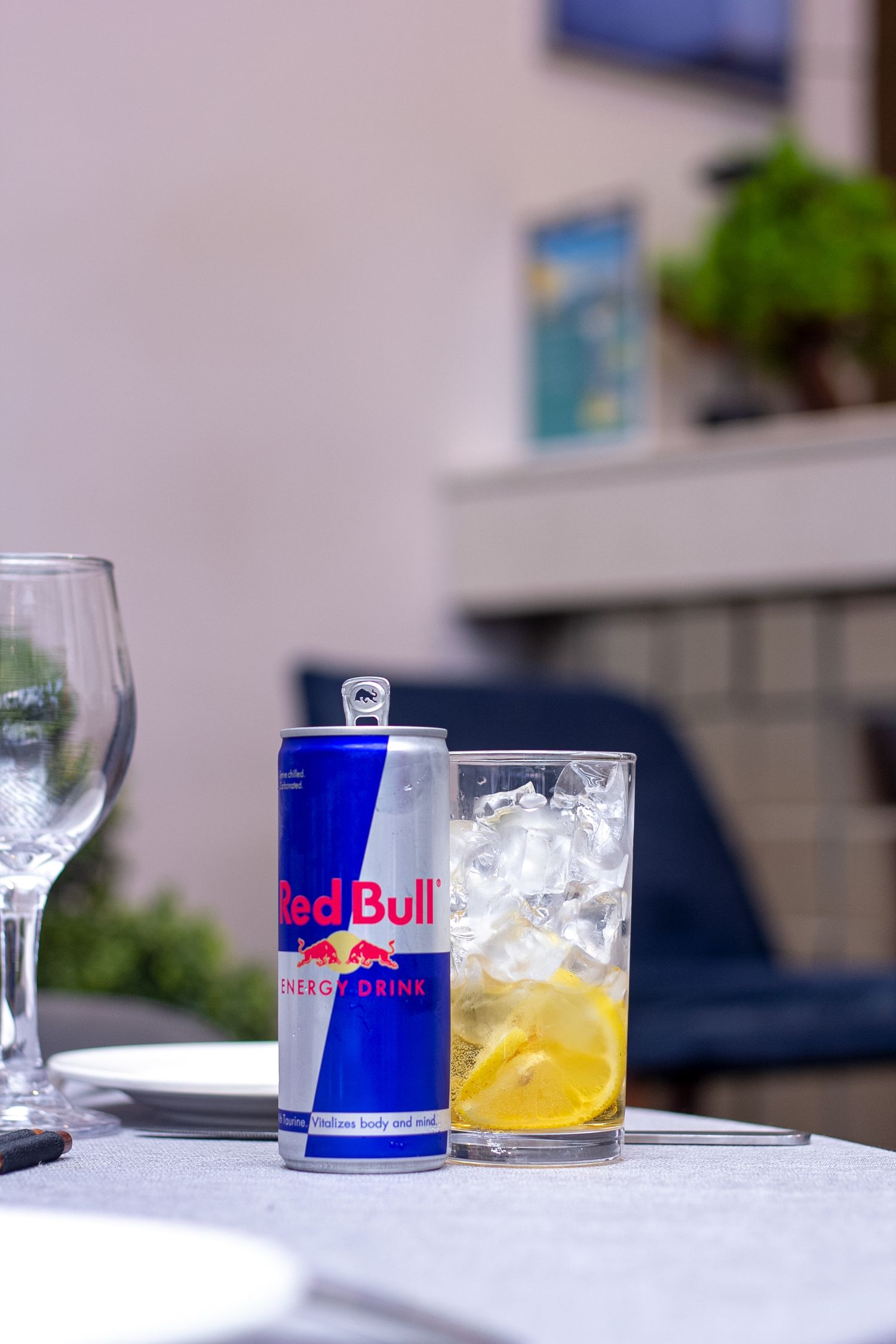 A can of Redbull beside a glass cup of Ice