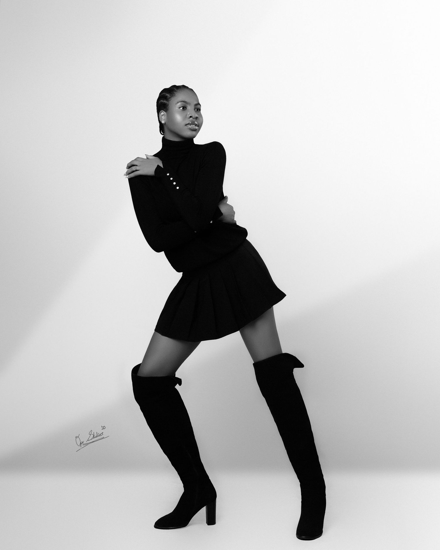 A black and white portrait of a beautiful Nigerian model standing and posing in a black turtle neck, black skirt and black knee high boots