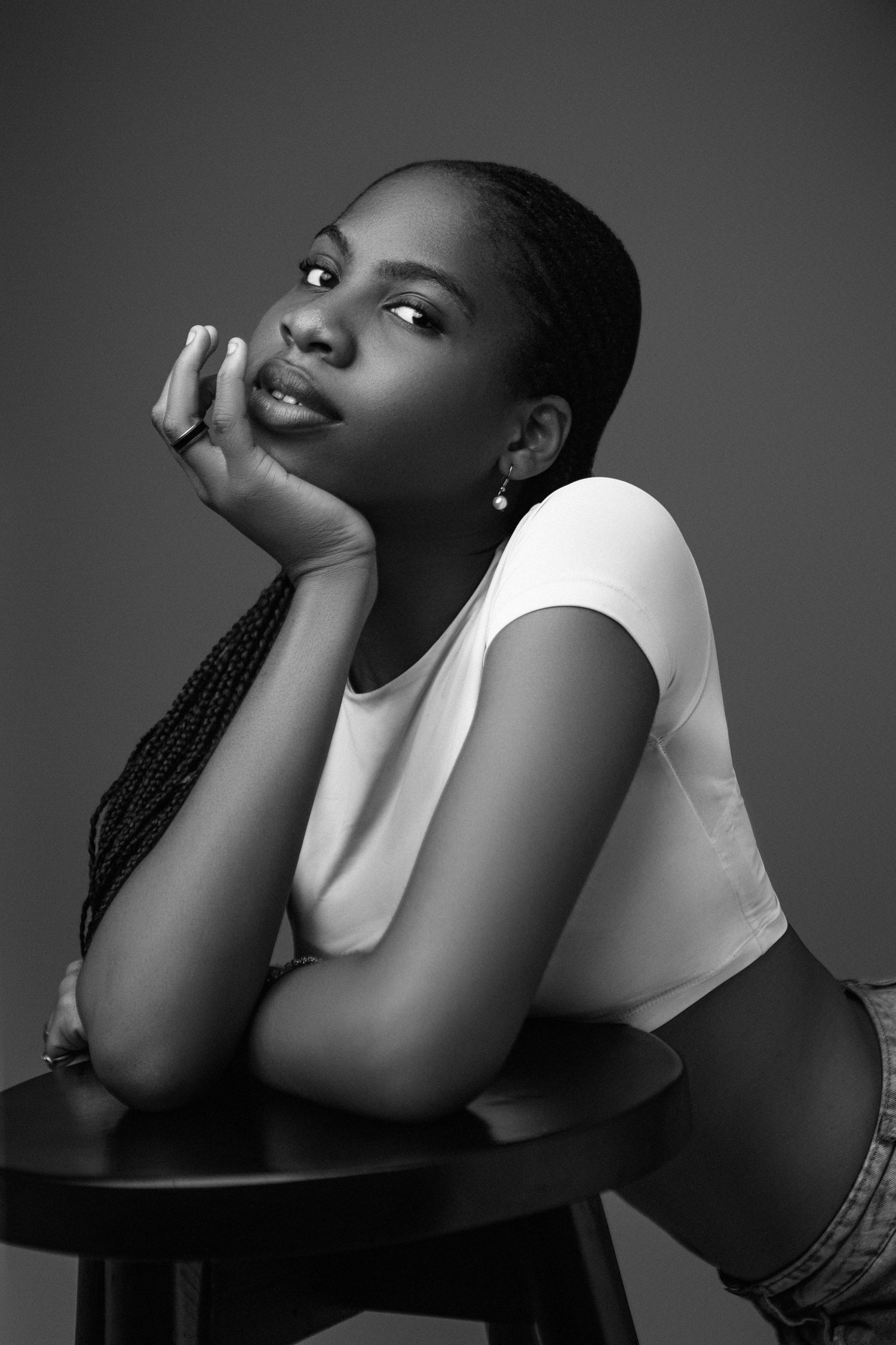 A black and white portrait of a beautiful Nigerian model leaning of a black stool
