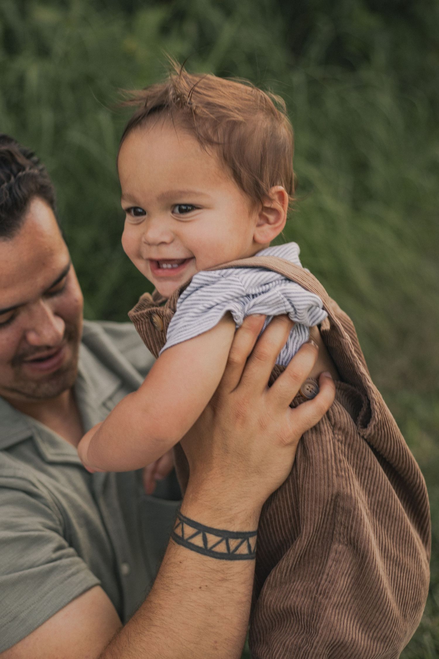 A dad holding up his young son who is smiling past the camera at his mom.
