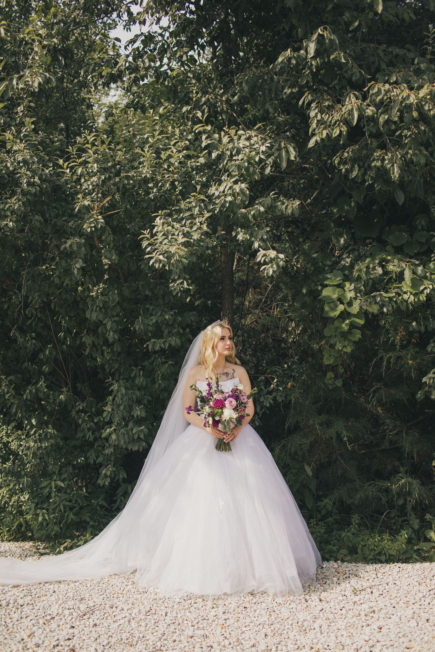 A bride staring off into the distance in a moody, woodsy setting.