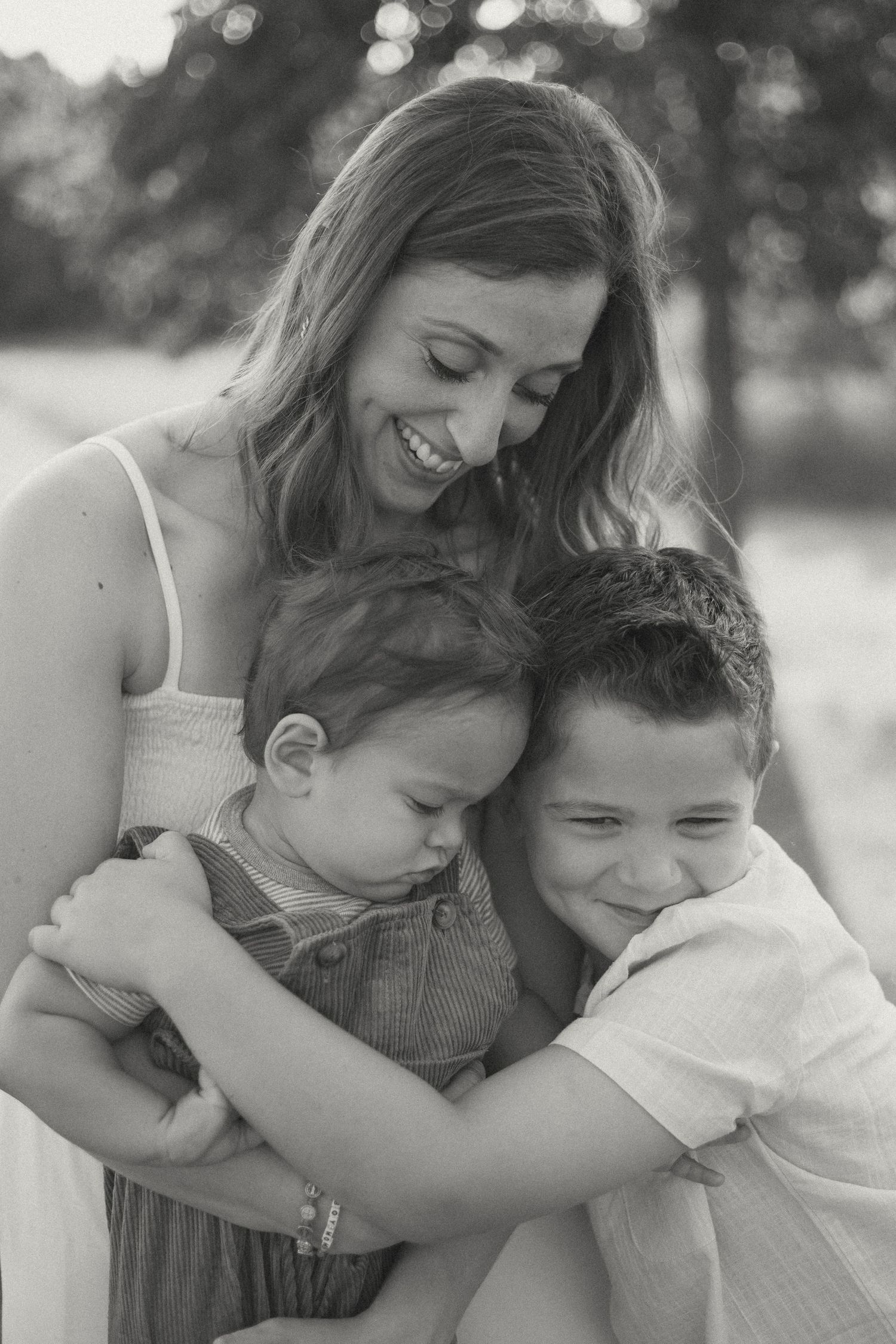 A mother with her two sons, looking down and smiling at her oldest while he hugs them.