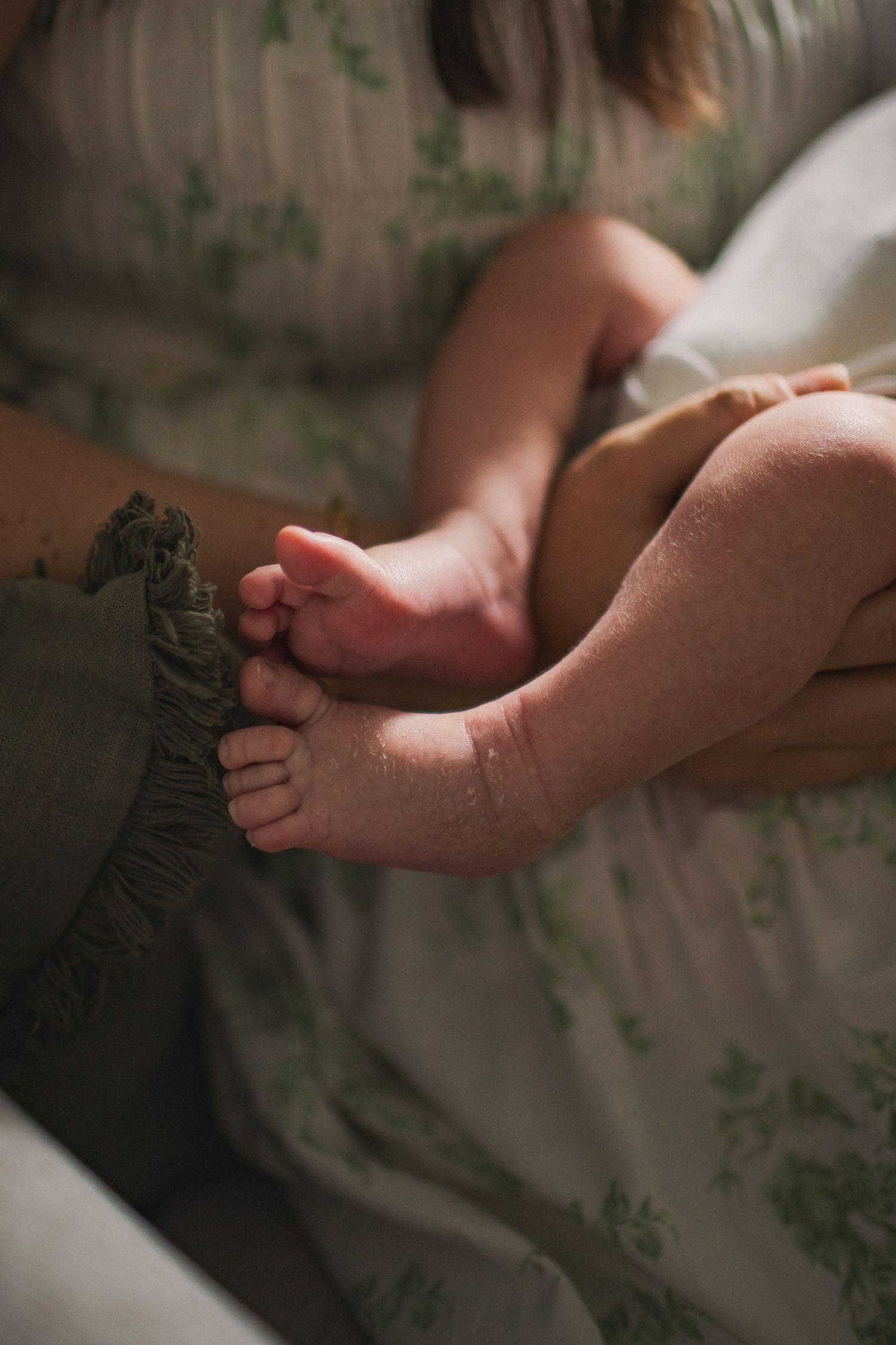 Moody newborn lifestyle session, with a close-up of a newborn baby's feet as his mother holds him in a rocking chair.
