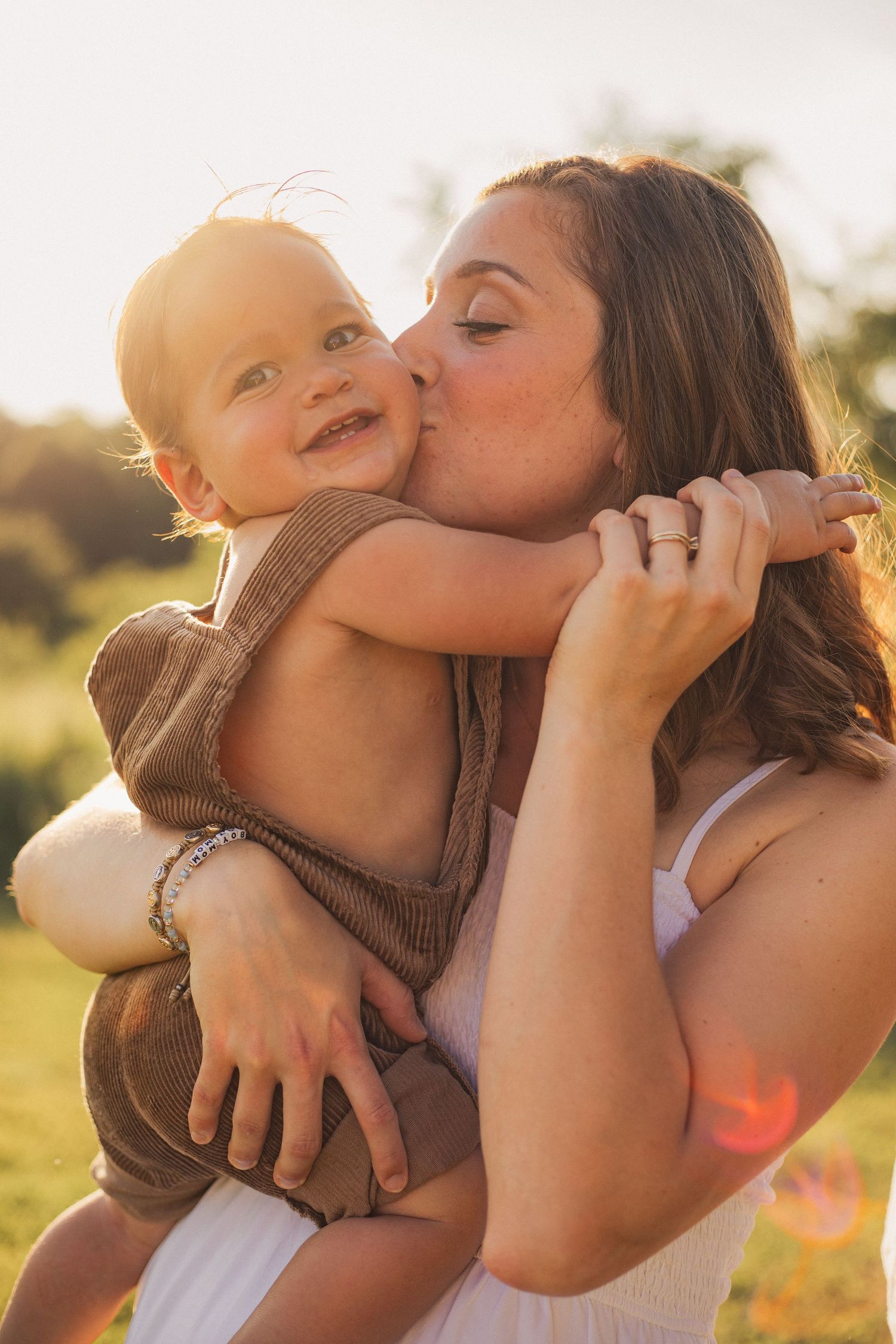 A mother kissing her little boy with the sunset glowing in the background.