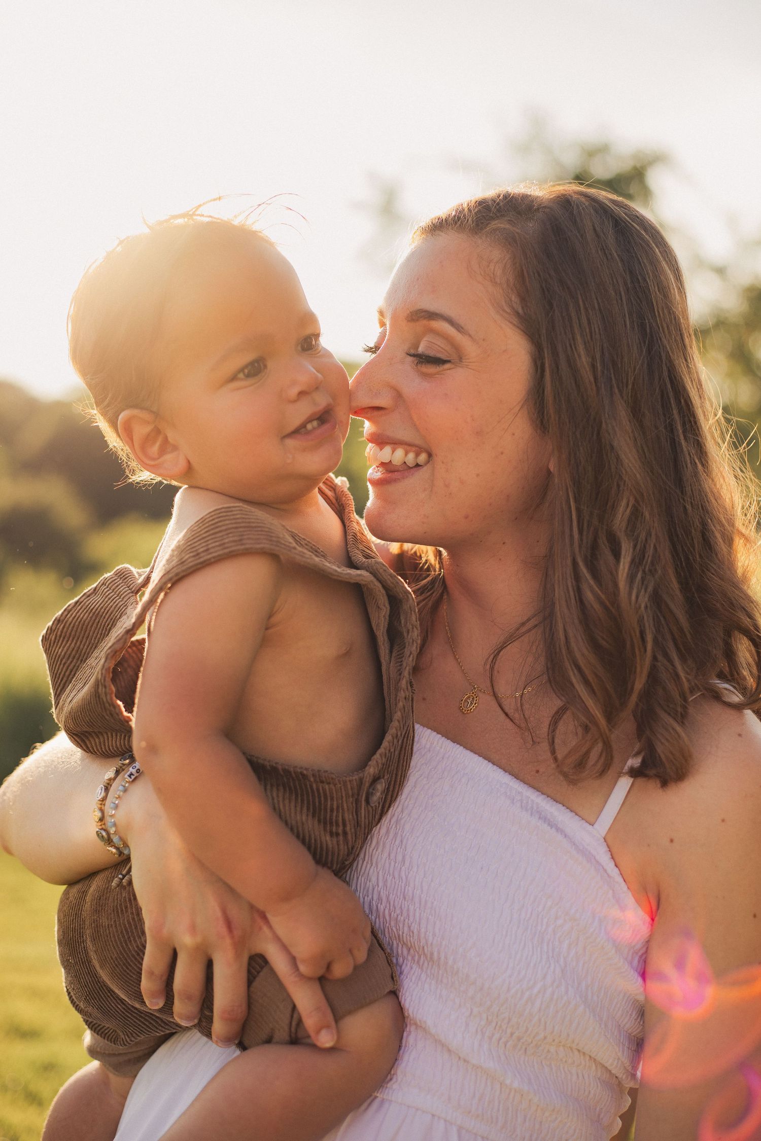 A mother smiling at her little boy with the sunset glowing in the background.