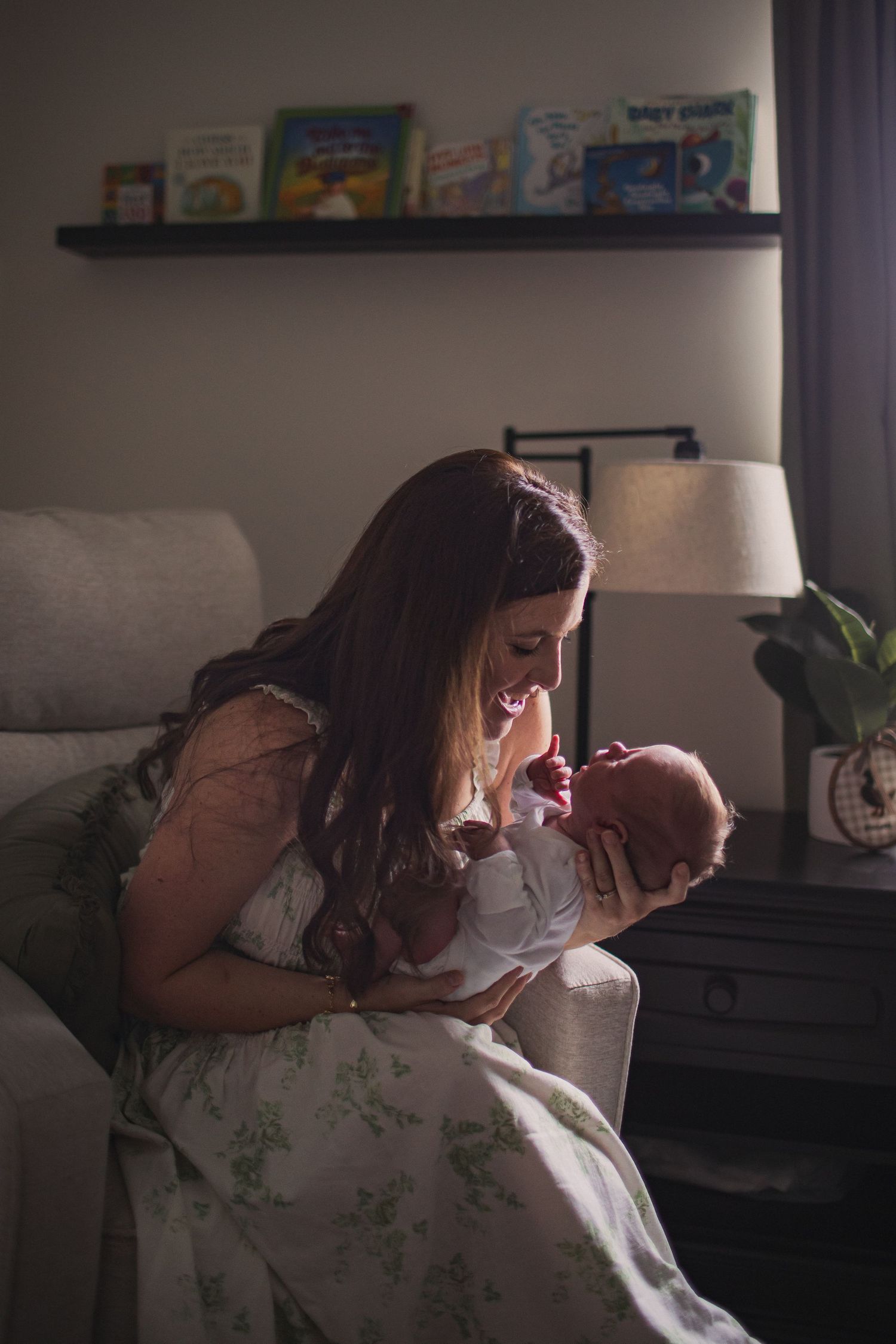 A mother smiling and talking to her newborn baby as she holds him in a rocking chair in a nursery.