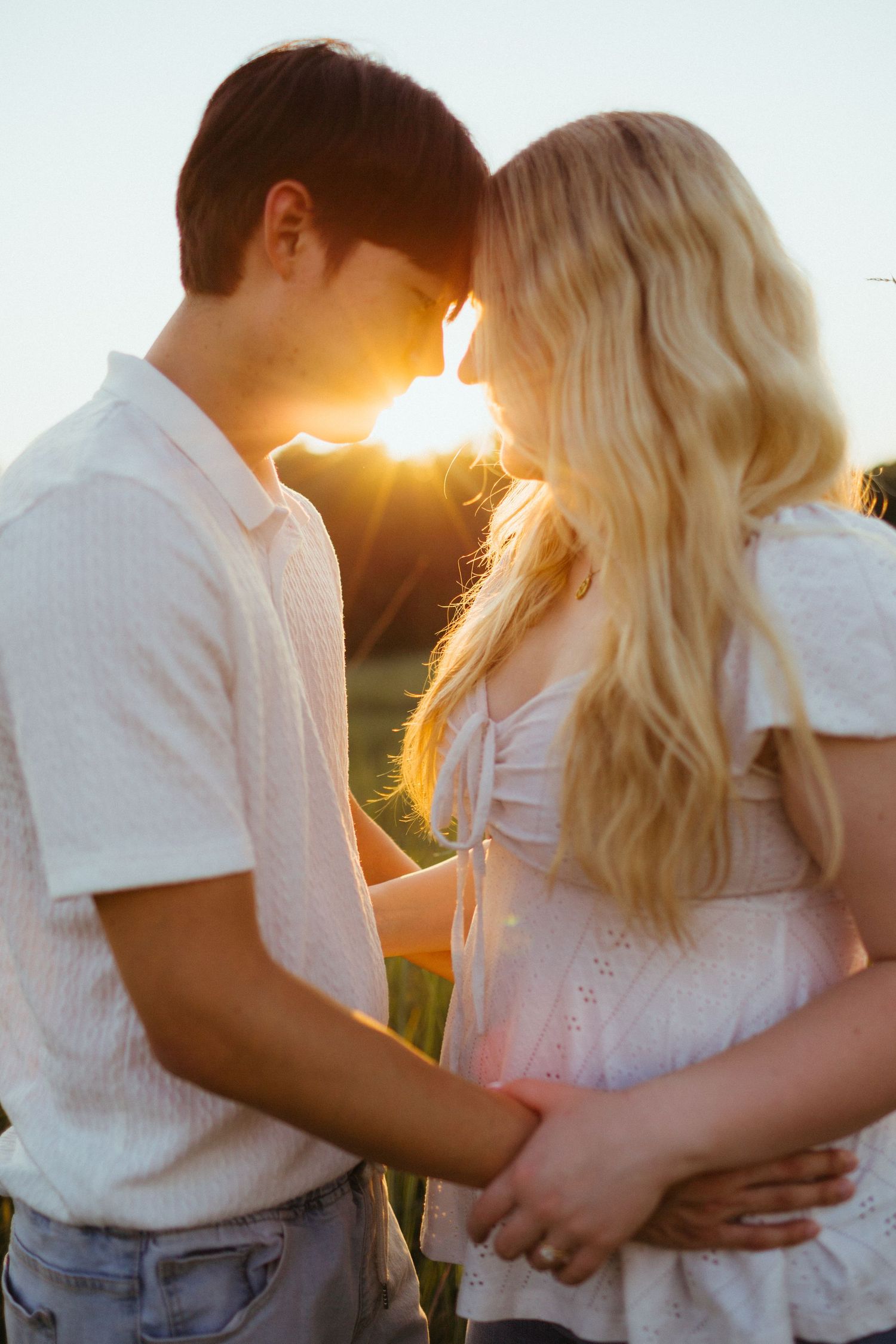 A young couple smiling at each other during a warm sunset engagement session.
