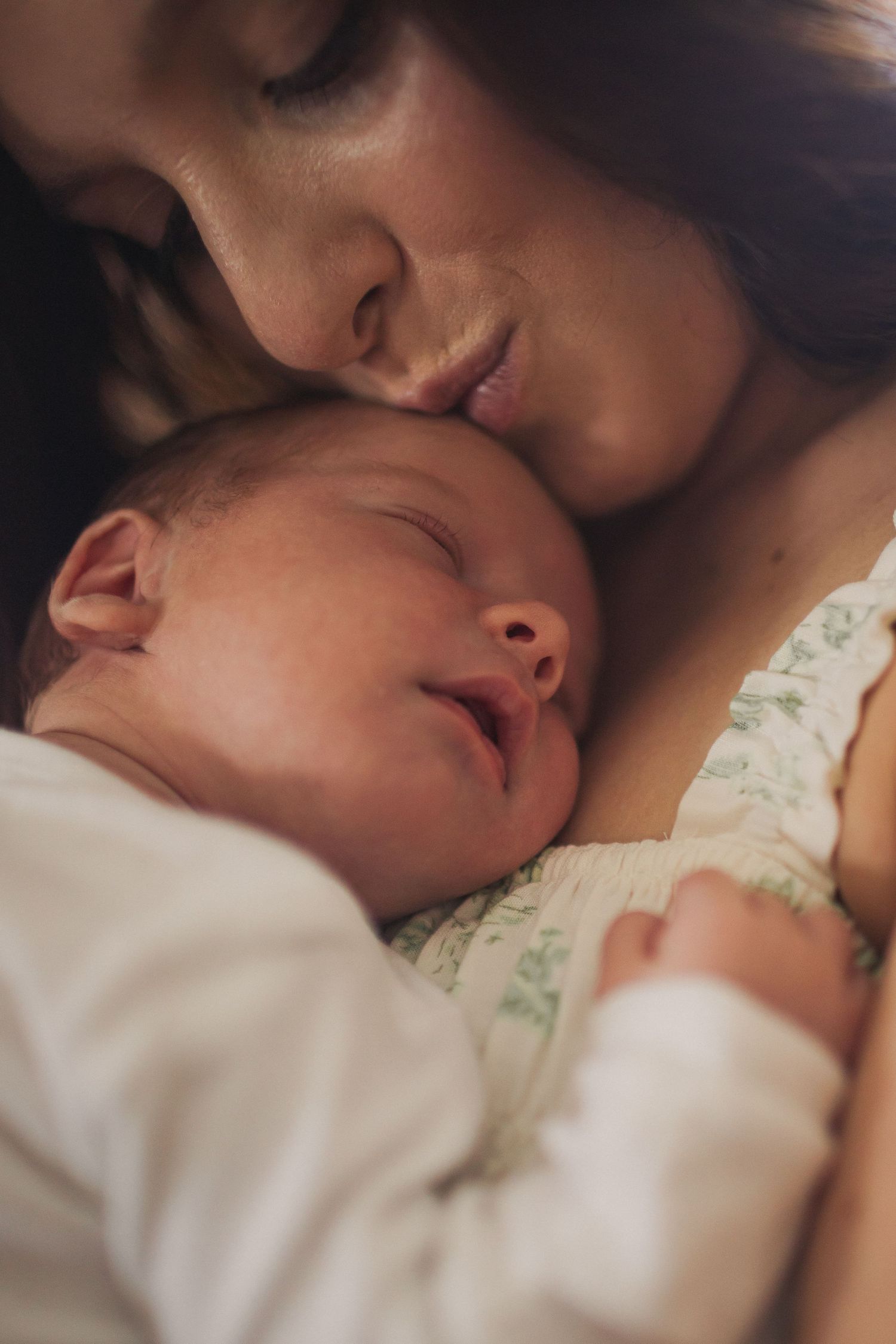 Closeup of a mother kissing the top of her newborn baby's head.