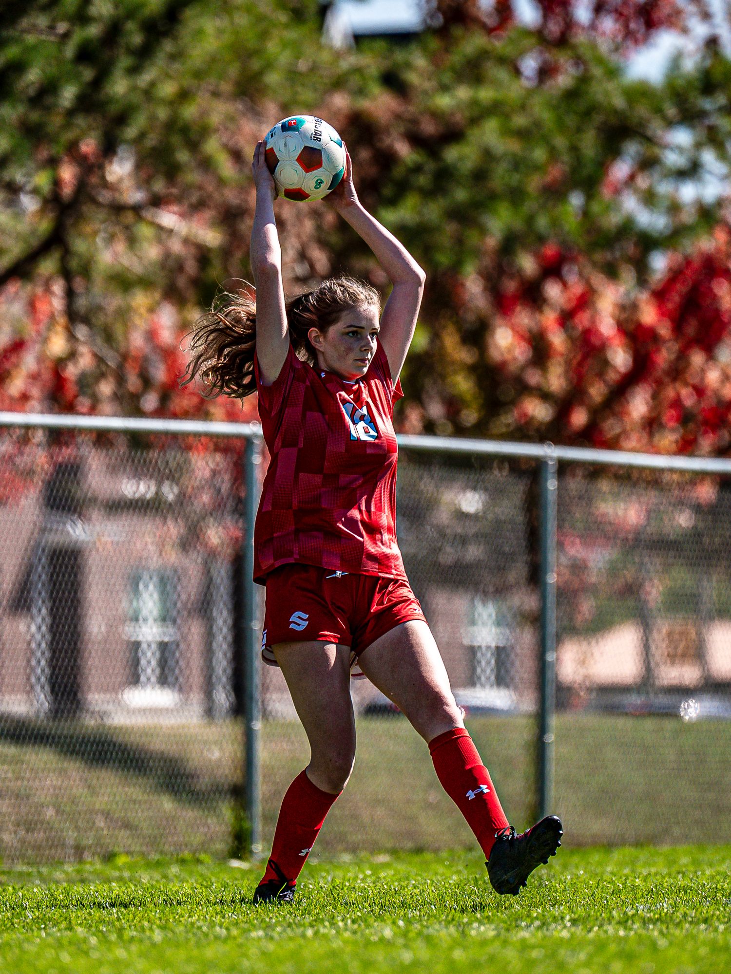 Soccer goalie in red uniform dives to make a save during practice on a sunny autumn day.