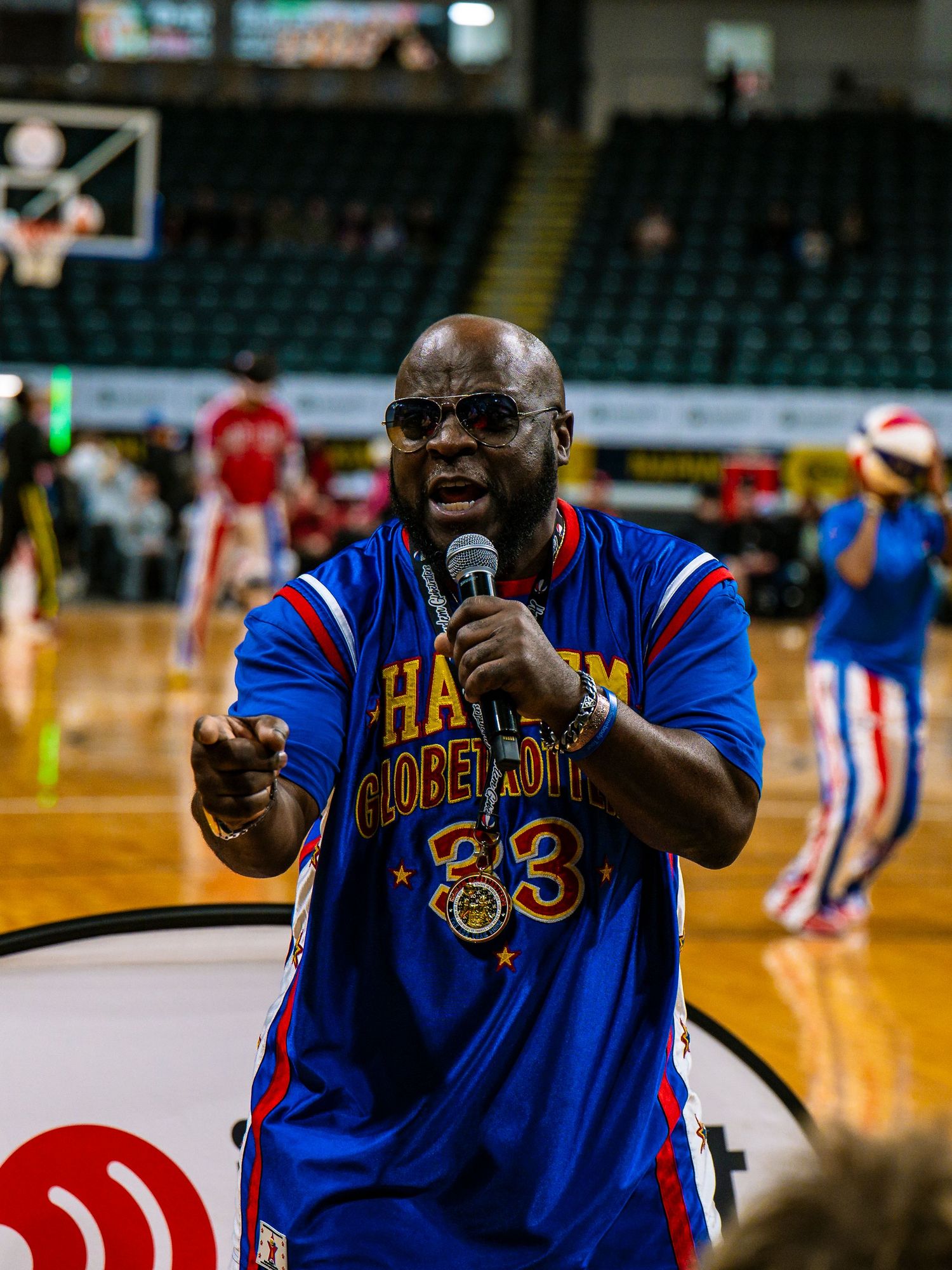 Basketball entertainer in blue and red uniform performs with microphone on court during halftime show.
