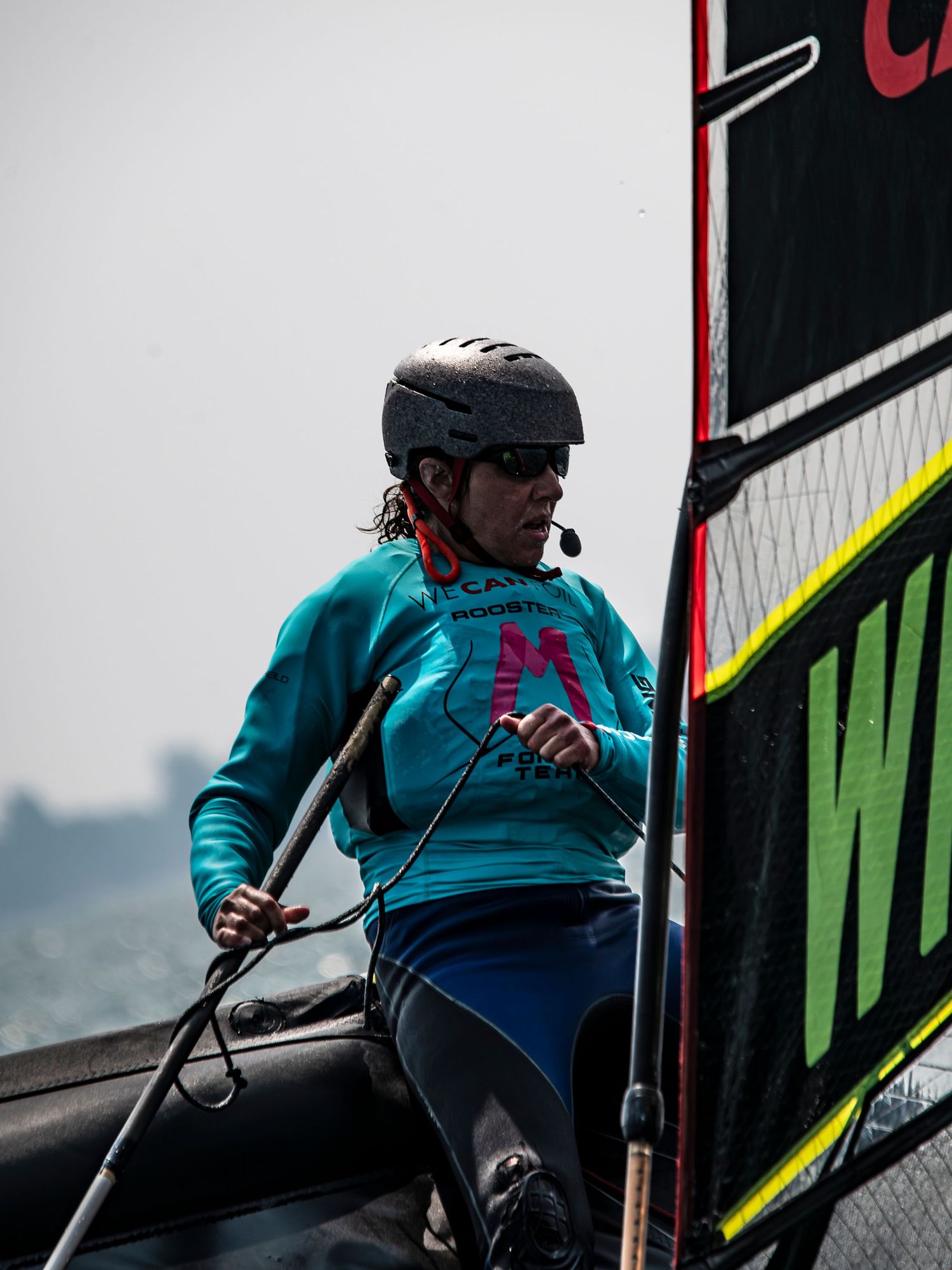 A delivery rider in a turquoise jacket and helmet rides up a ramp while making a food delivery.