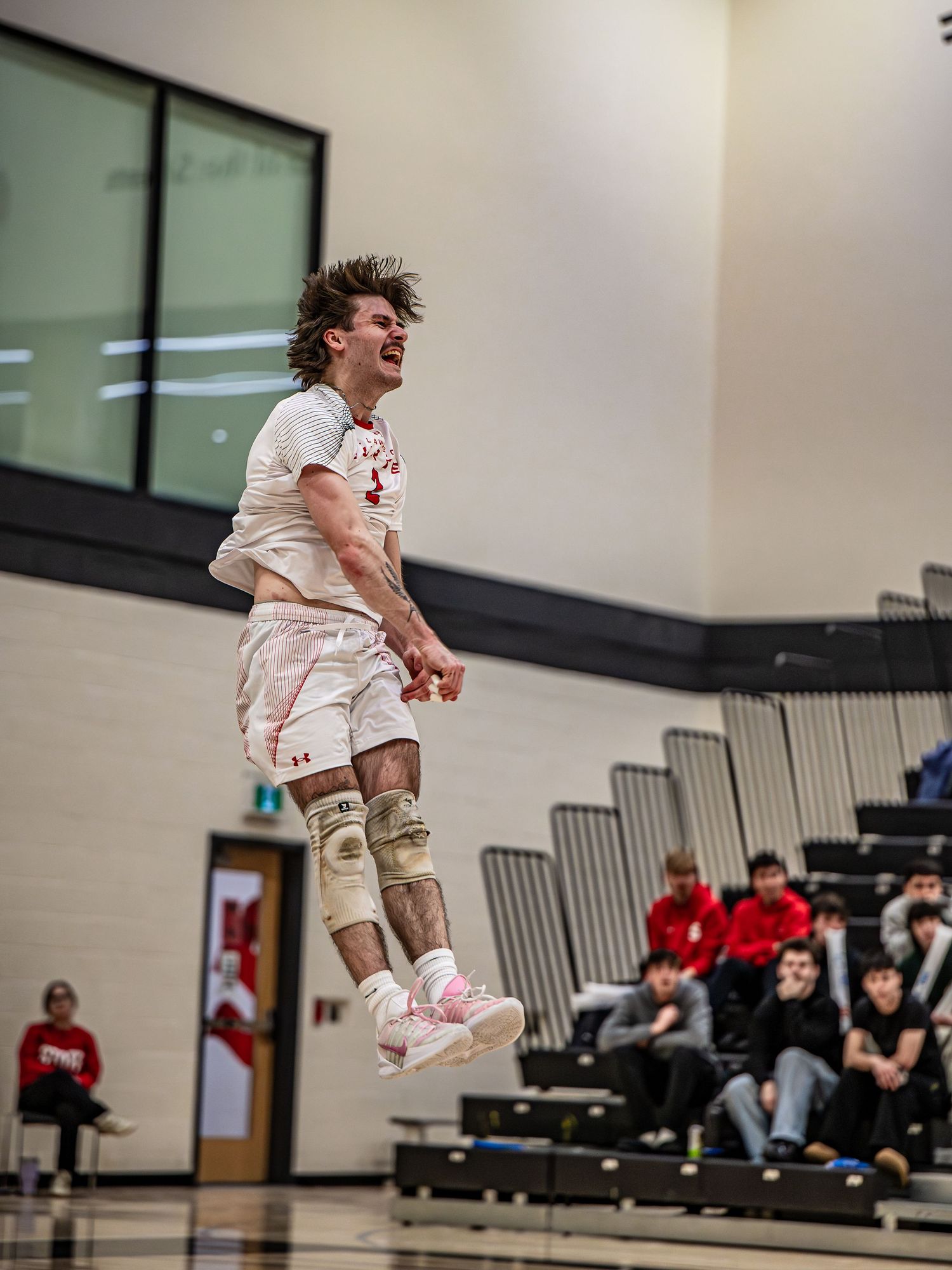 Basketball player leaps high in the air during an indoor game while spectators watch from the bleachers.