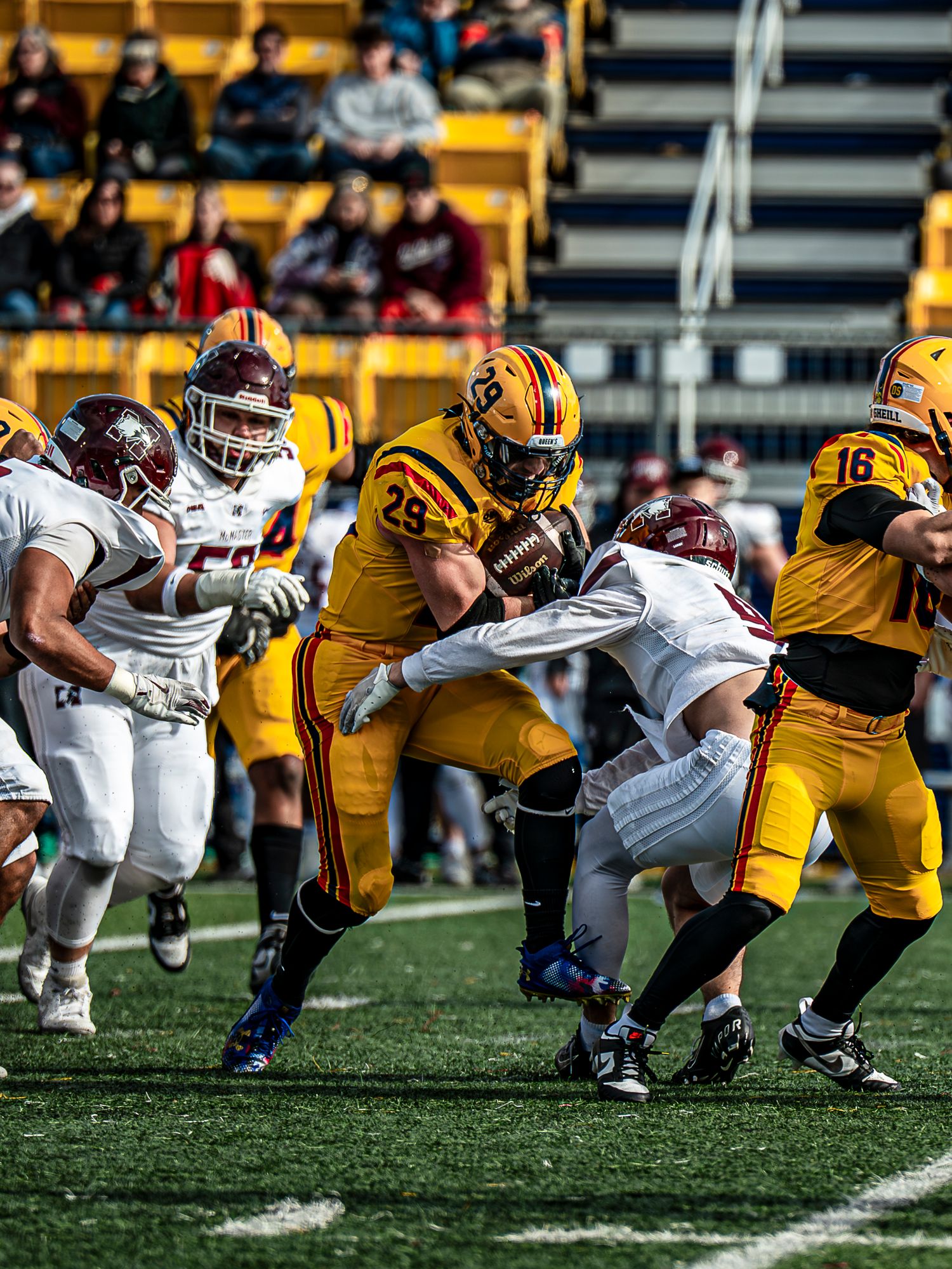 Football teams in yellow and white uniforms clash during intense line of scrimmage play.