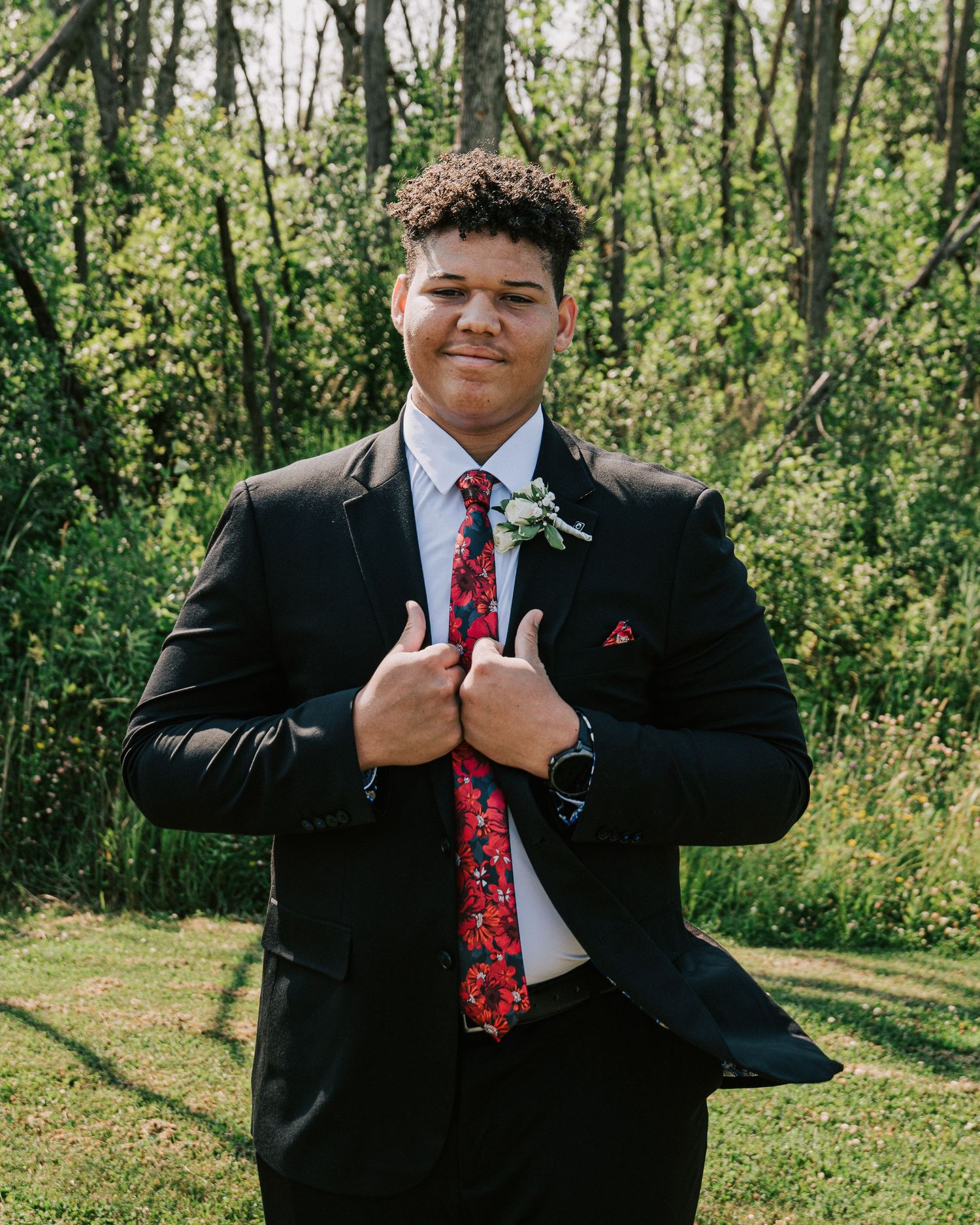 A sequence of photos shows someone in a black suit and red tie adjusting their tie against a green outdoor background.