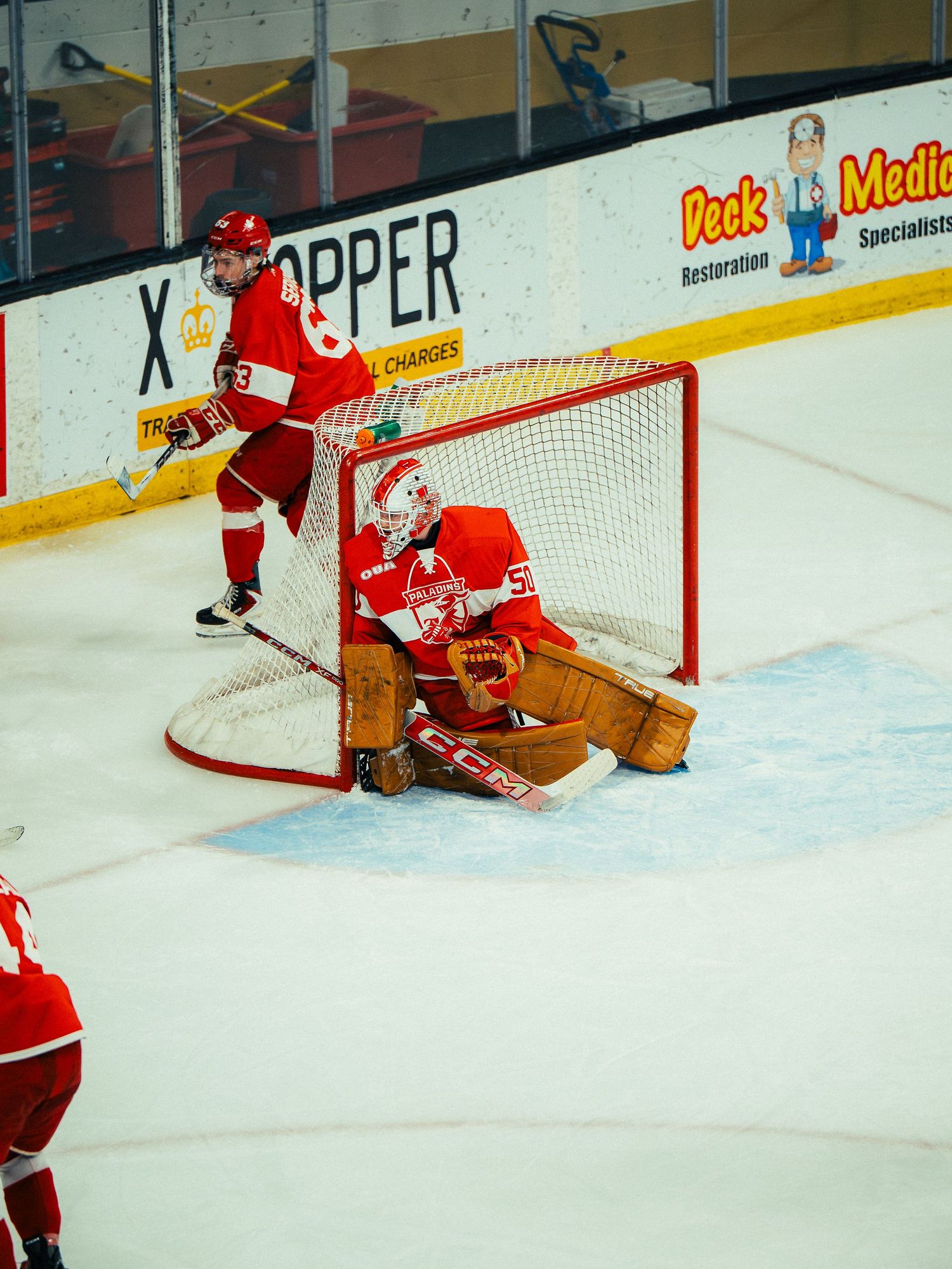 Hockey goalie in red uniform defending net during game on ice rink.