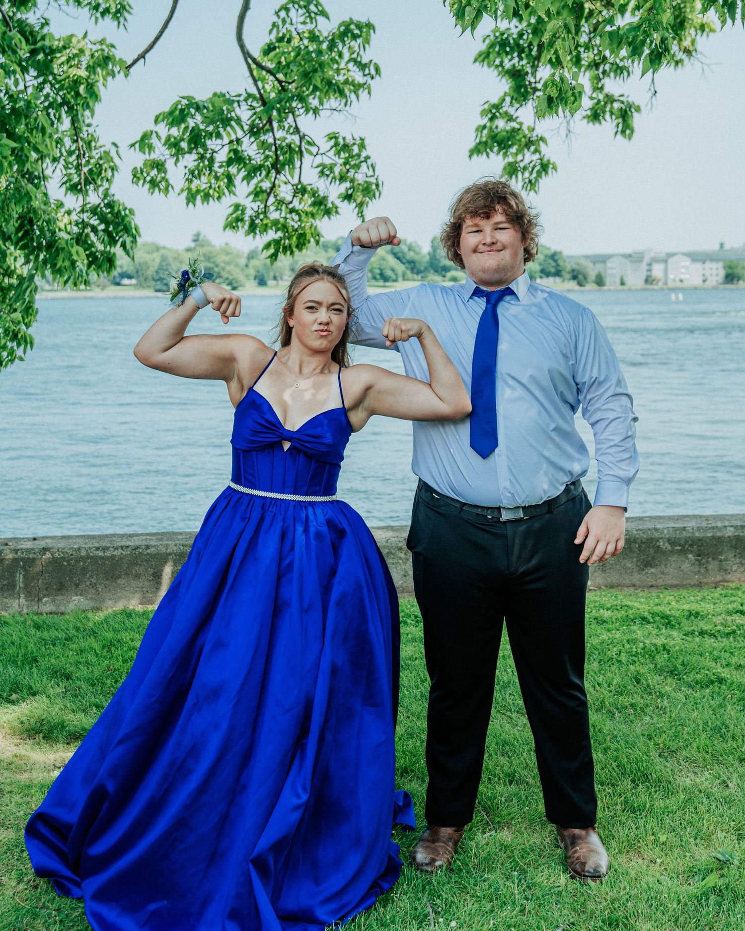 A couple in blue dress and grey attire poses playfully in a series of photos by the waterfront.