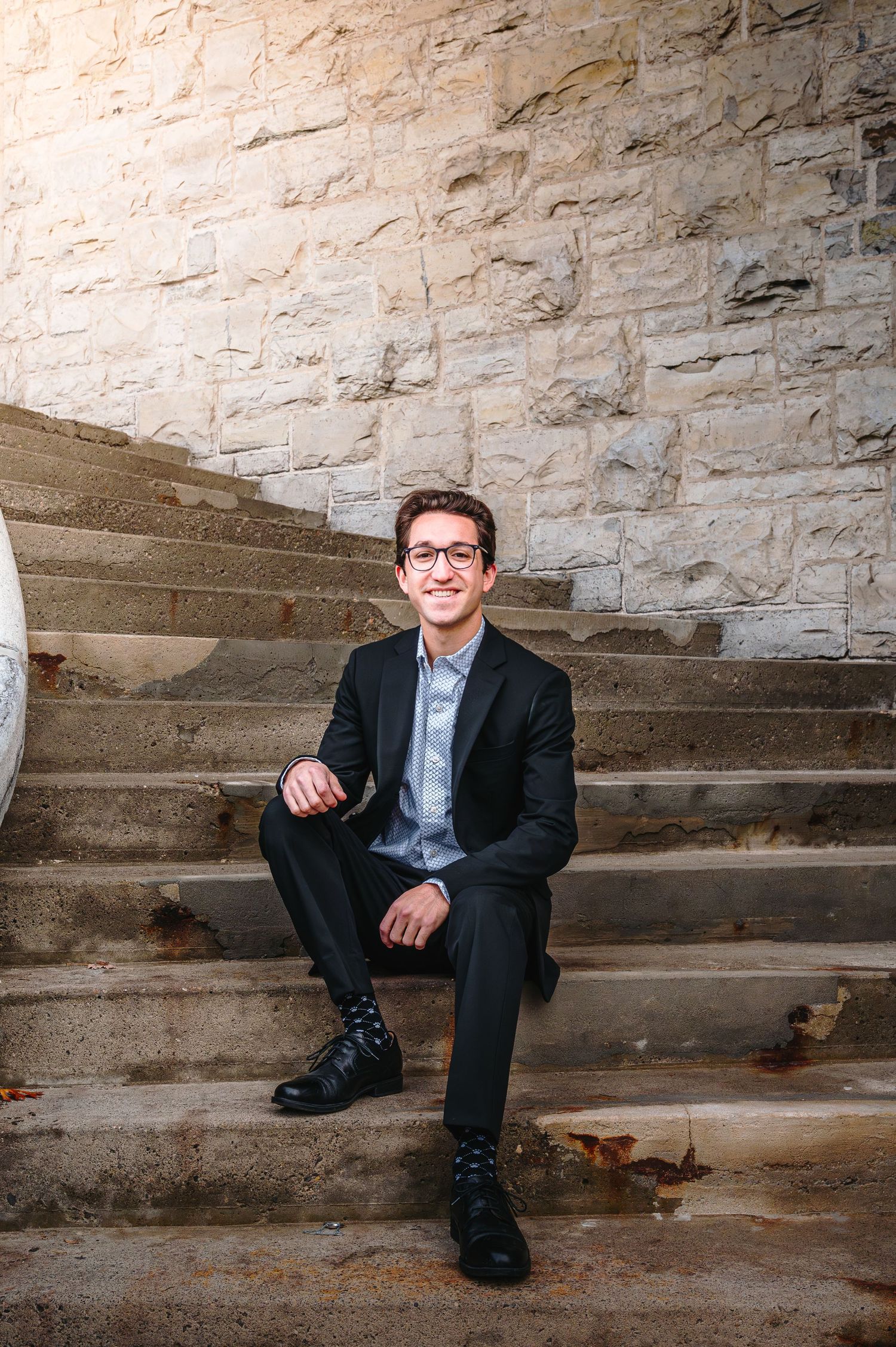 Professional portrait series showing someone seated on stone steps against a textured limestone wall.