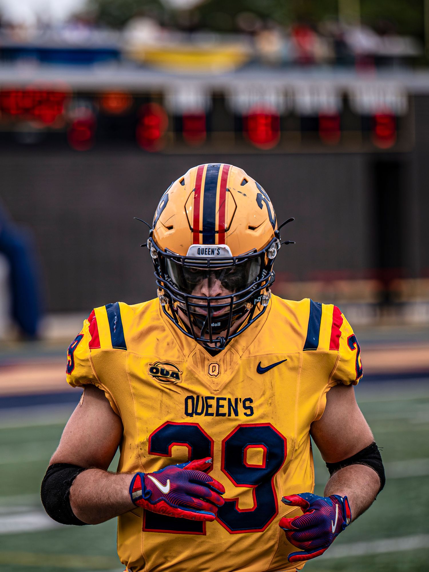 Football player in yellow Queen's jersey number 29 stands ready on field.