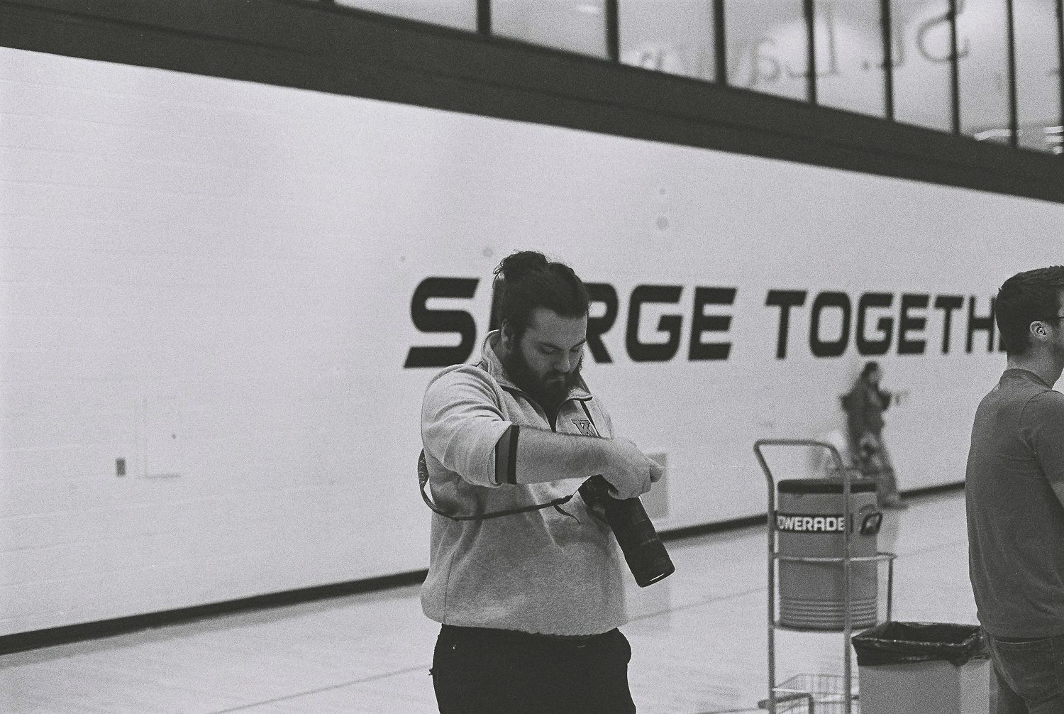 Black and white photo of a man checking his watch in a gym with a Surge Together banner on the wall.