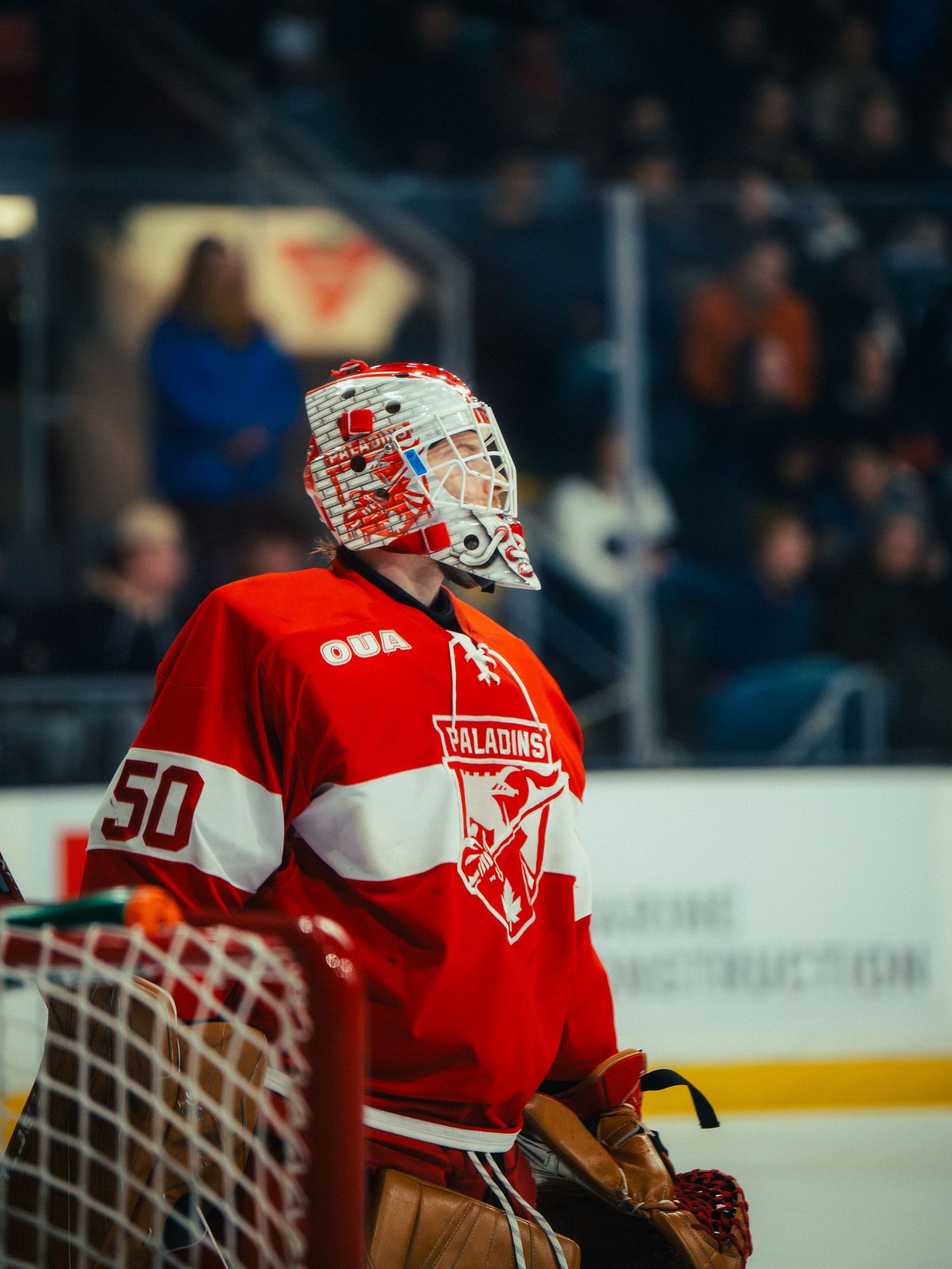 Hockey goalie in red and white jersey with number 50 standing near the net during a game.