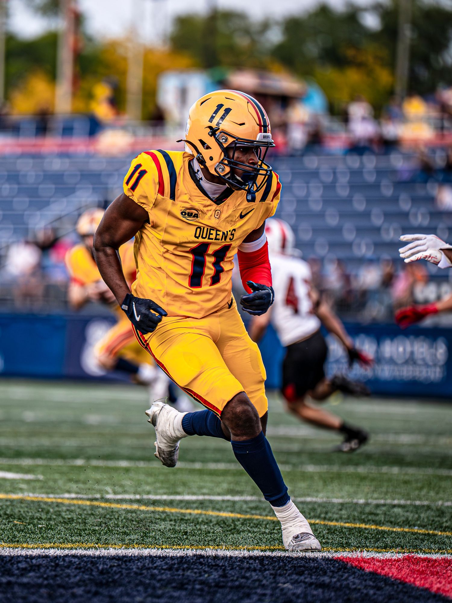 Football player in yellow uniform runs with determination during game on artificial turf.