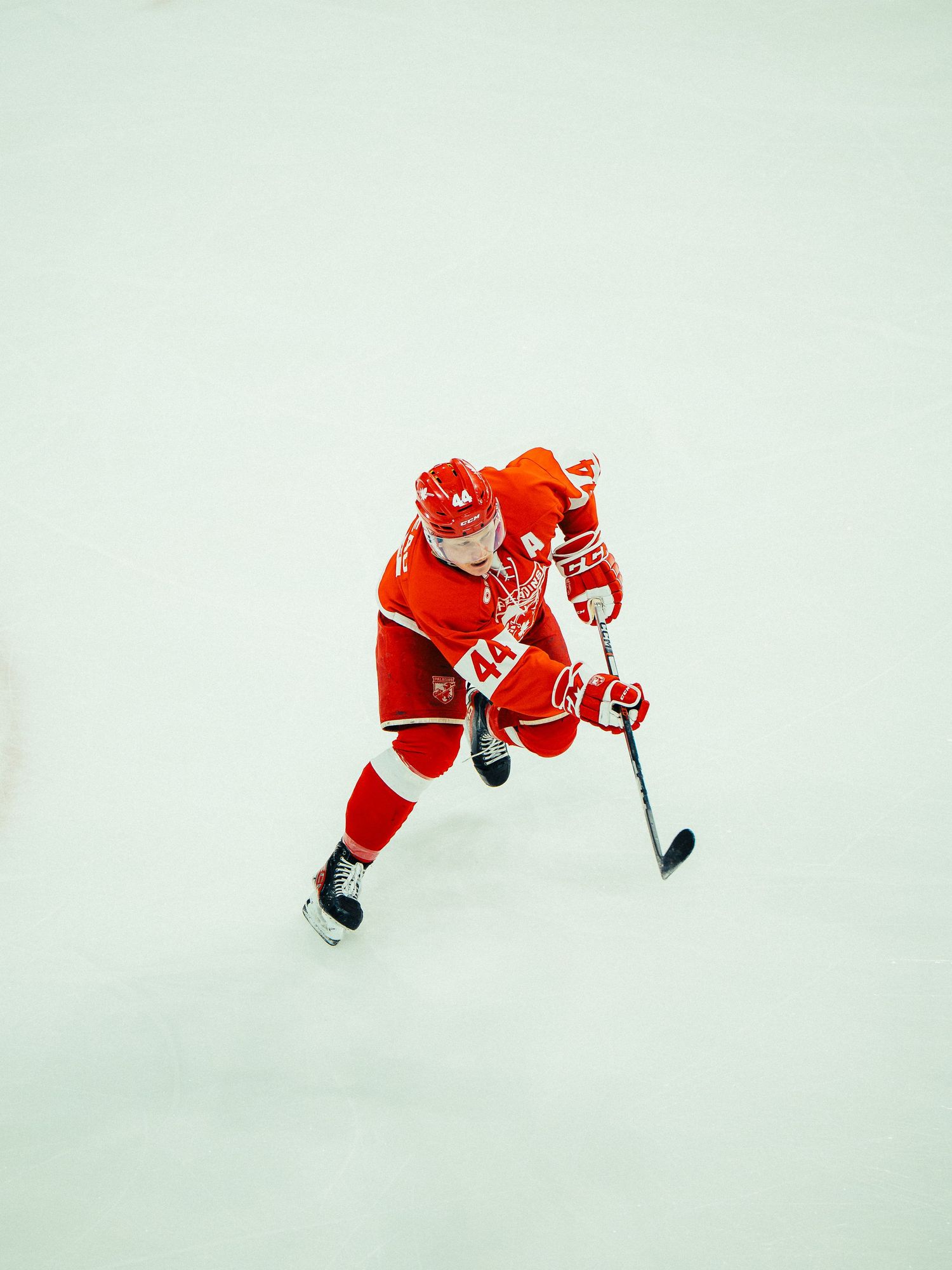 Hockey player in red jersey skates on ice with stick during competitive match.