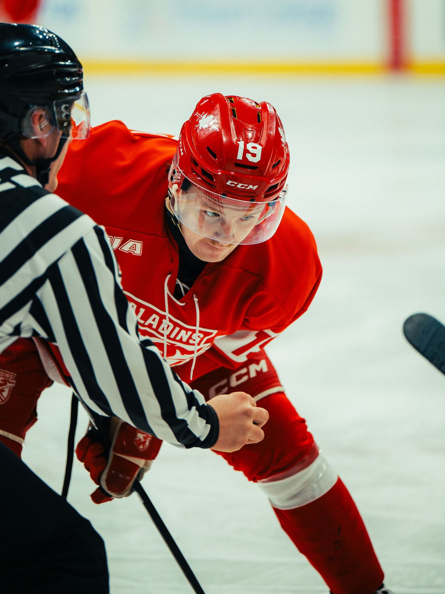 Hockey player in red uniform faces off against referee on ice rink.