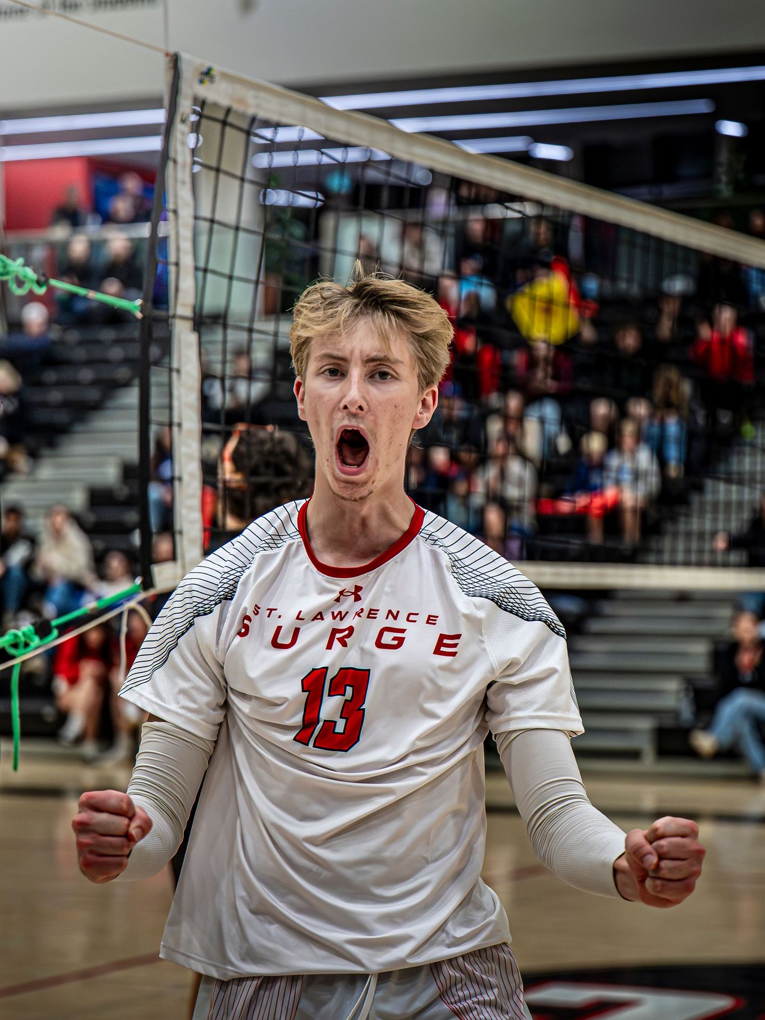 Volleyball player in white jersey number 13 celebrates with intense emotion during indoor match.