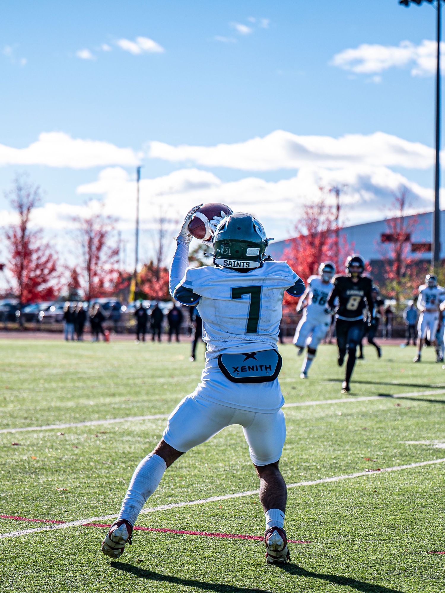 Football player in white uniform stretches during practice on sunny grass field.