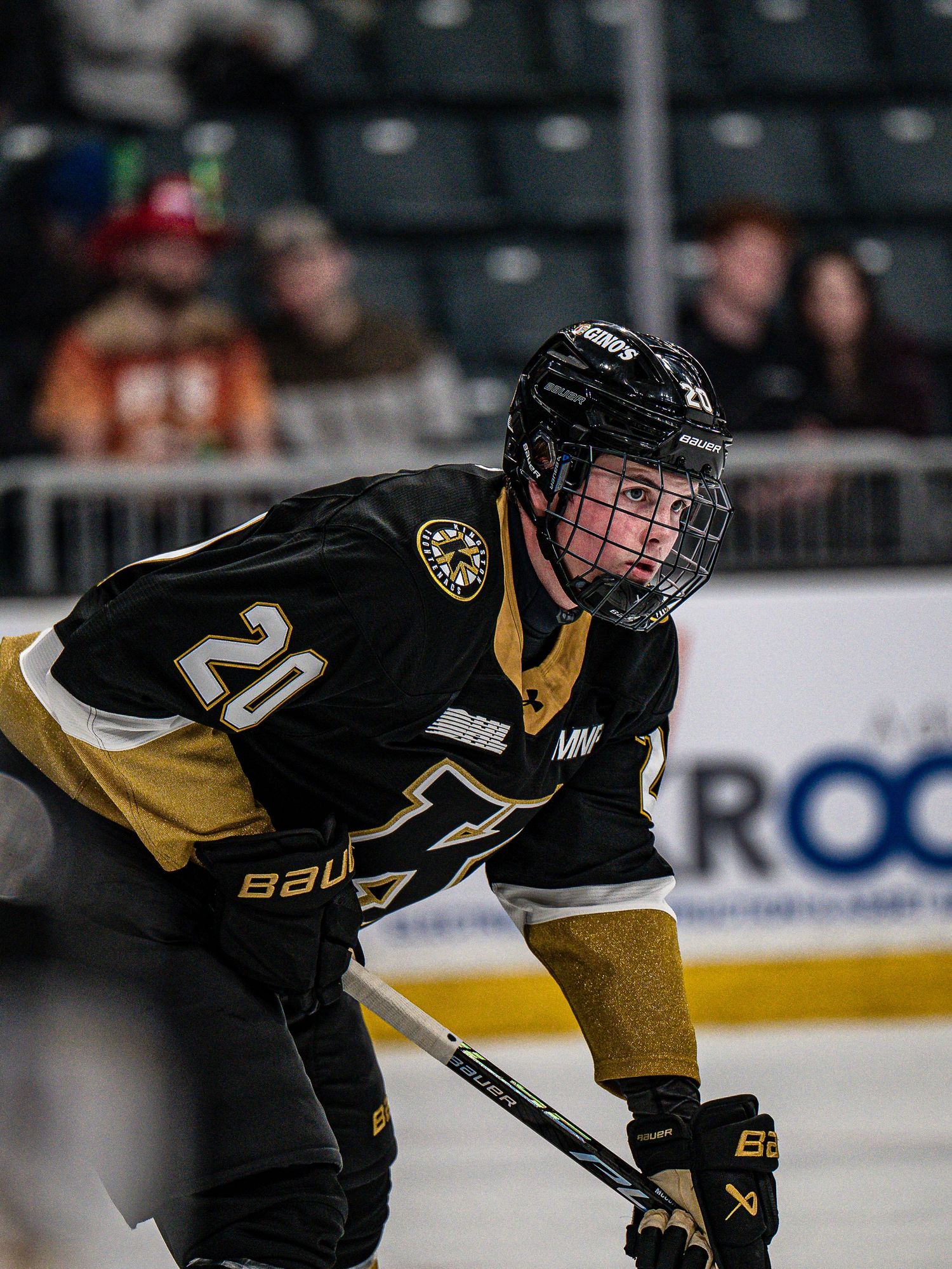 Hockey player in black and gold uniform number 20 crouches in ready position during game action.